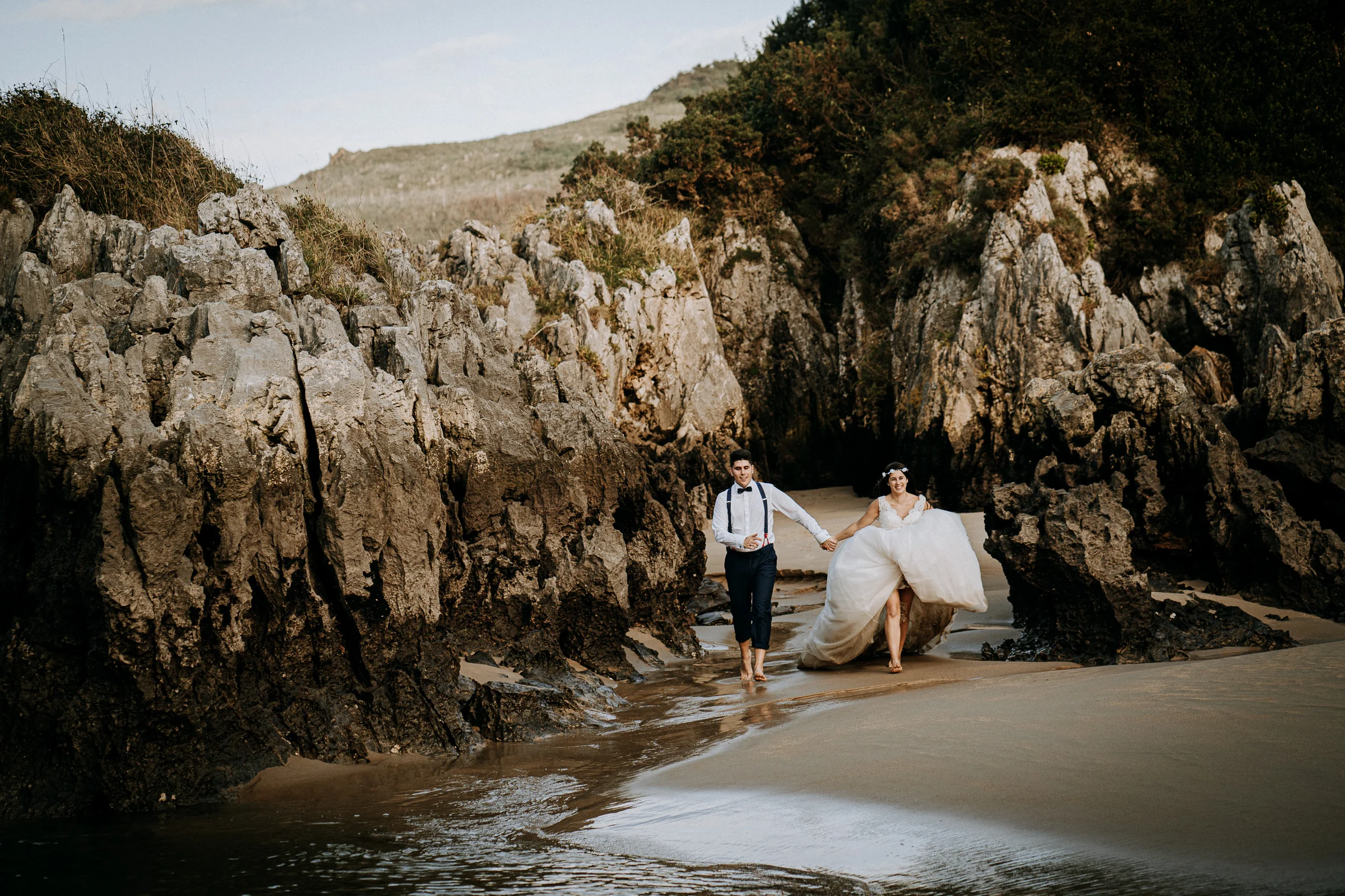 Pareja jugando y caminando por la playa durante una sesión de postboda en El Molino, cerca de Llanes, Asturias.