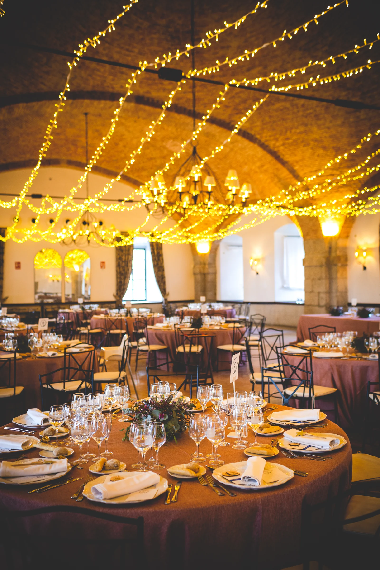 Salon del banquete iluminado con guirnaldas, fotografía de boda en el Castillo de Viñuelas.
