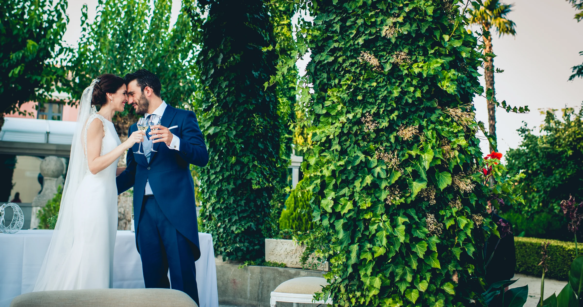 Novios abrazados junto a una columna cubierta de hiedra, fotografía de boda en el Castillo de Viñuelas.