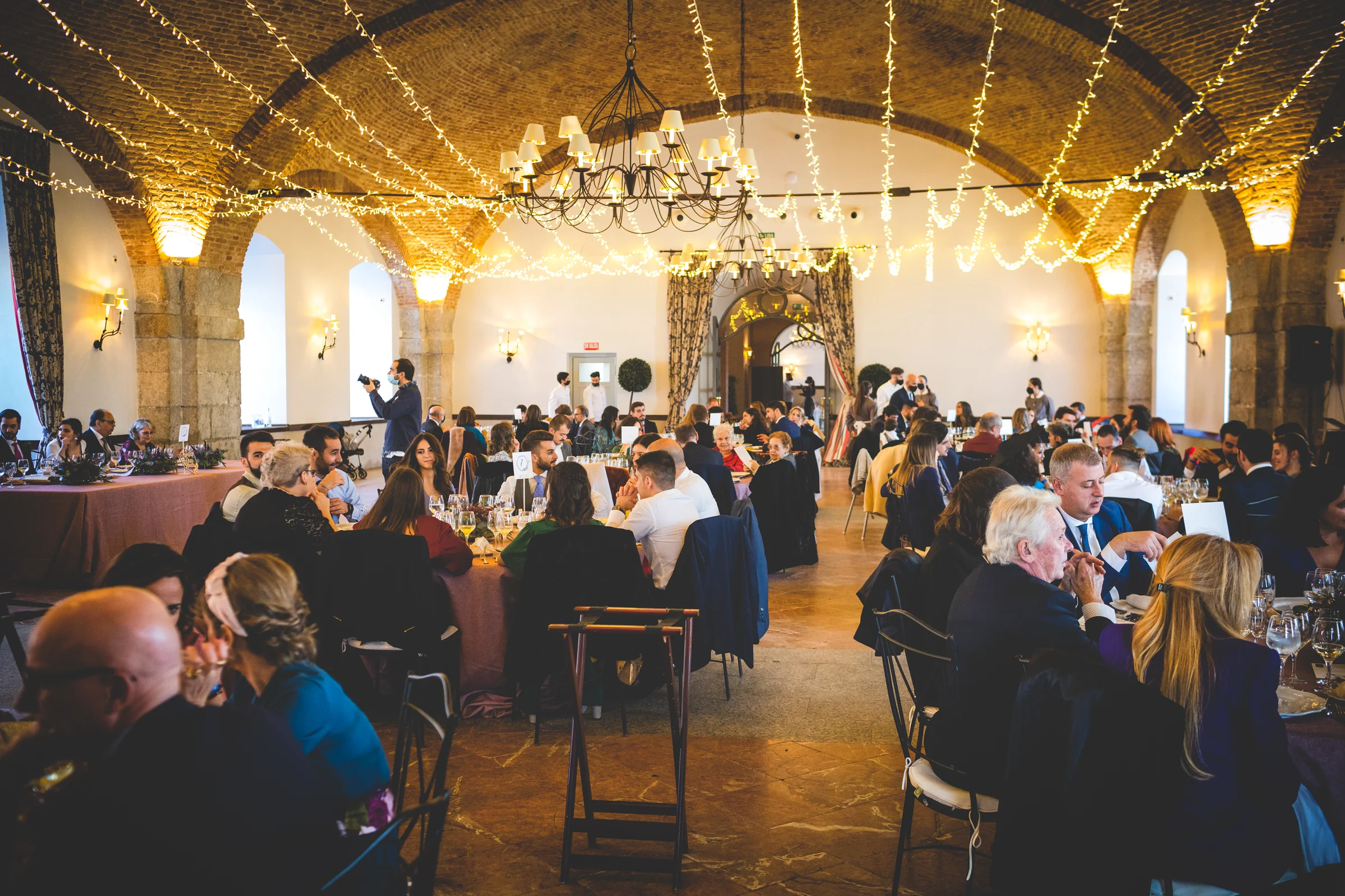 Banquete celebrado bajo guirnaldas de luces, fotografía de boda en el Castillo de Viñuelas.