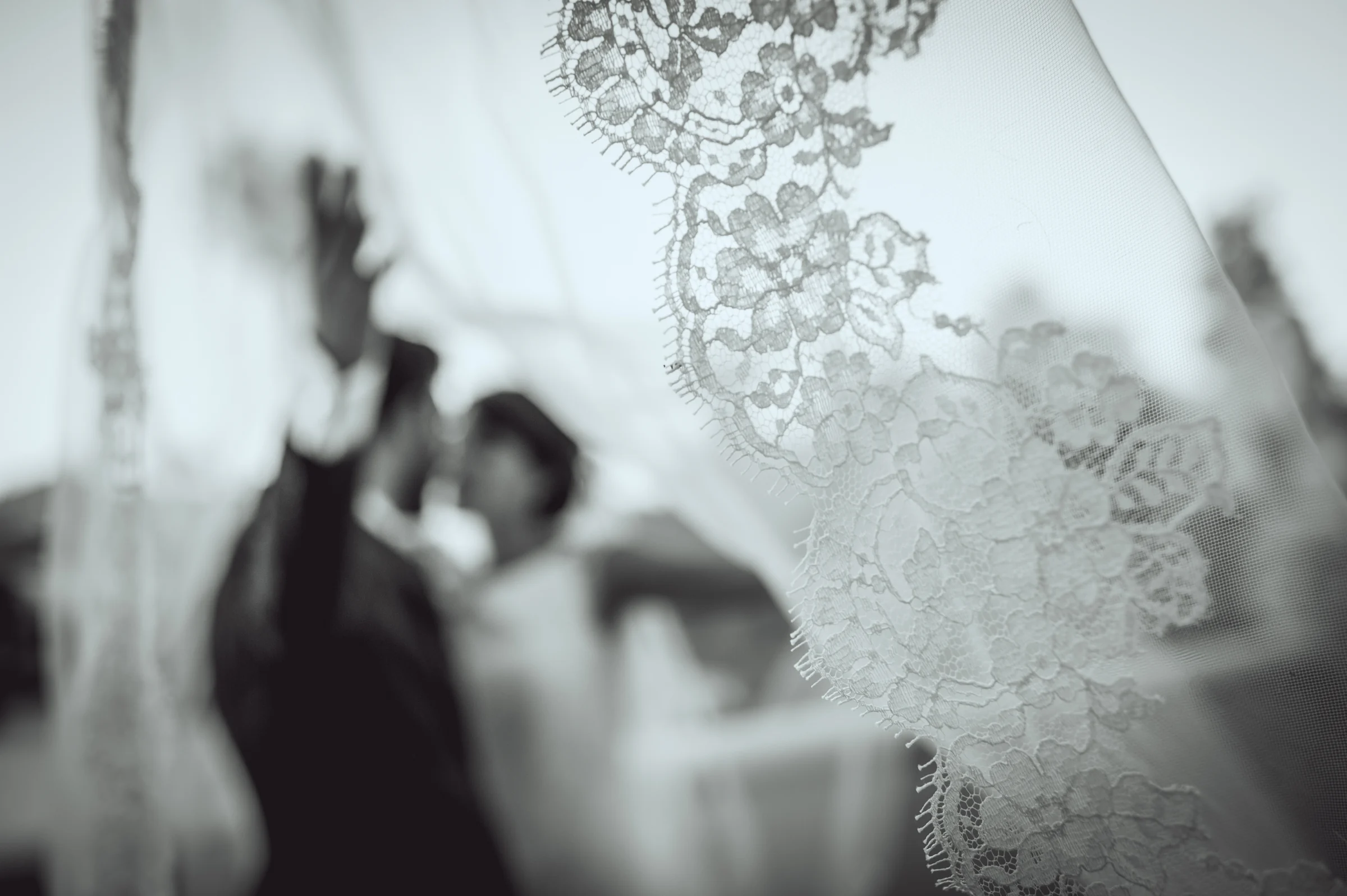 Detalle del encaje del velo con los novios al fondo, fotografía de boda en el Castillo de Viñuelas.