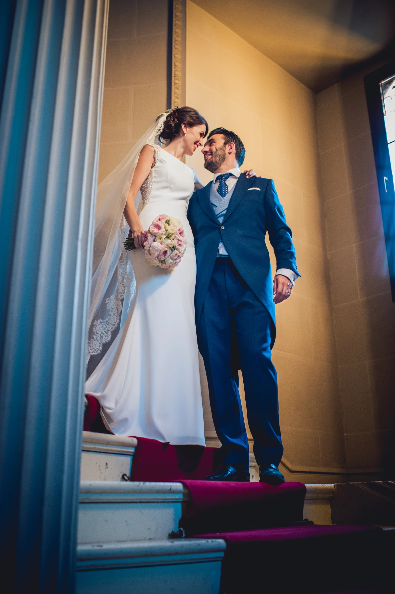Novios bajando por una escalera interior, fotografía de boda en el Castillo de Viñuelas.