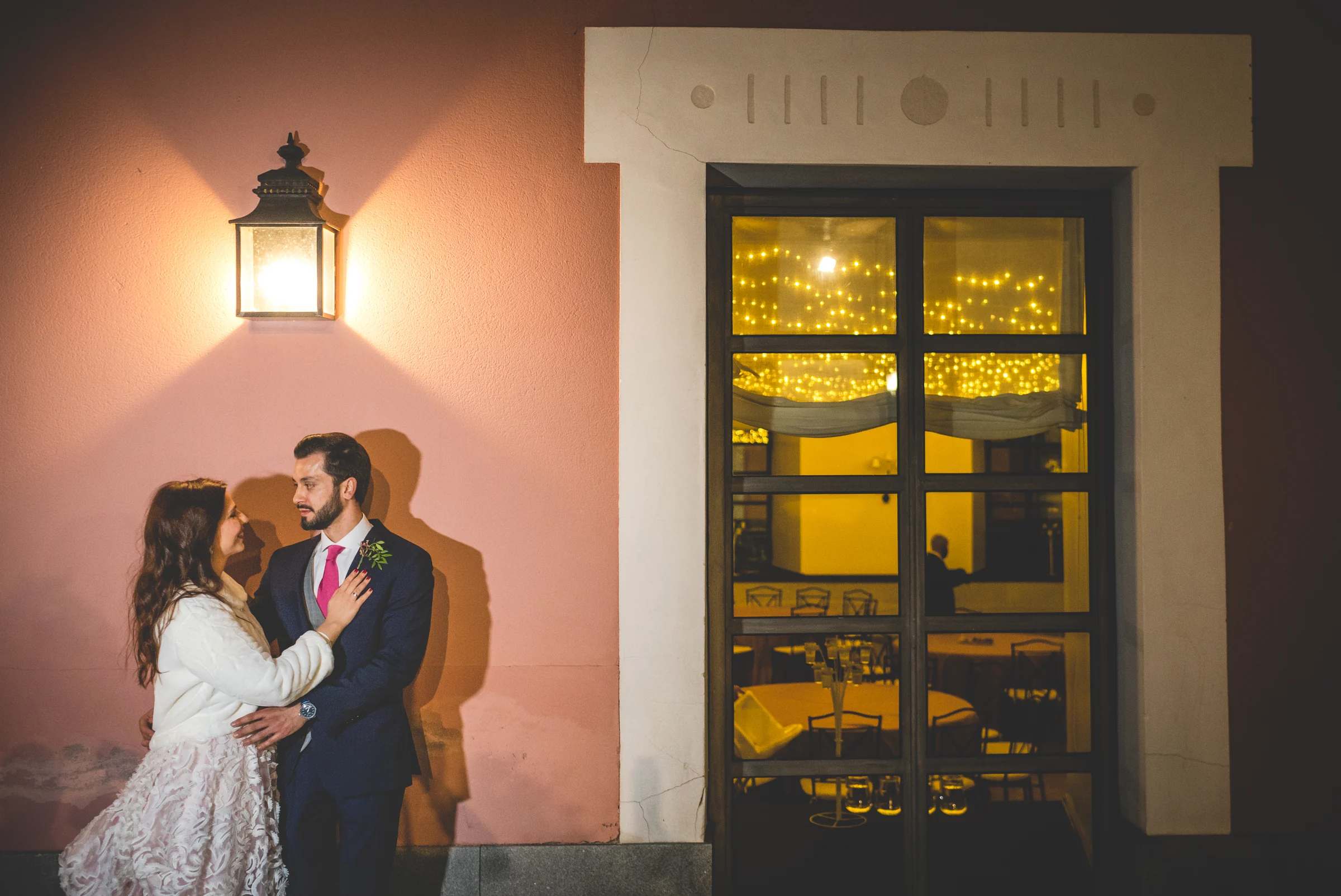 Novios besándose junto a una puerta iluminada, fotografía de boda en el Castillo de Viñuelas.