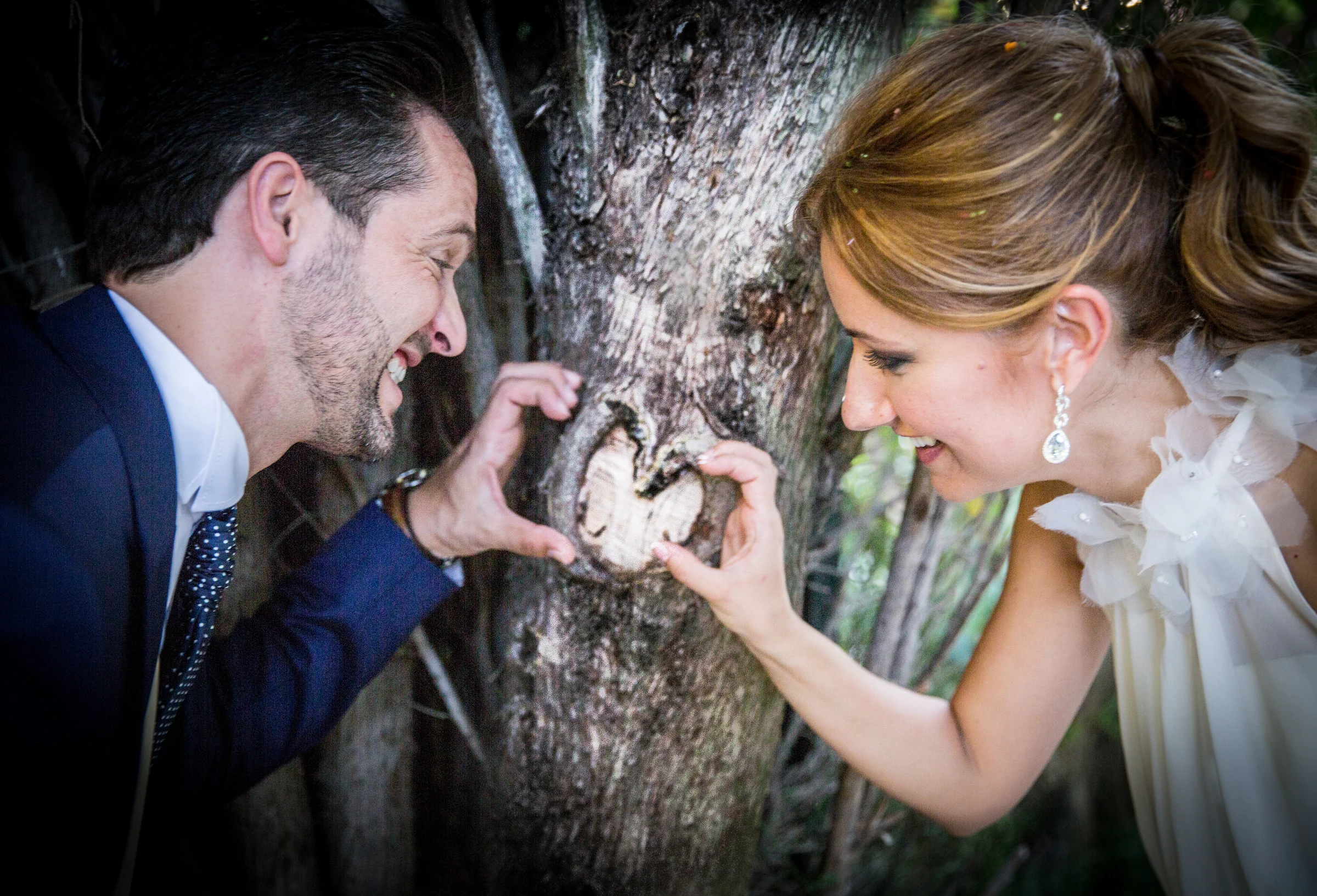 Novios formando un corazón con las manos junto a un árbol en Cigarral de las Mercedes.