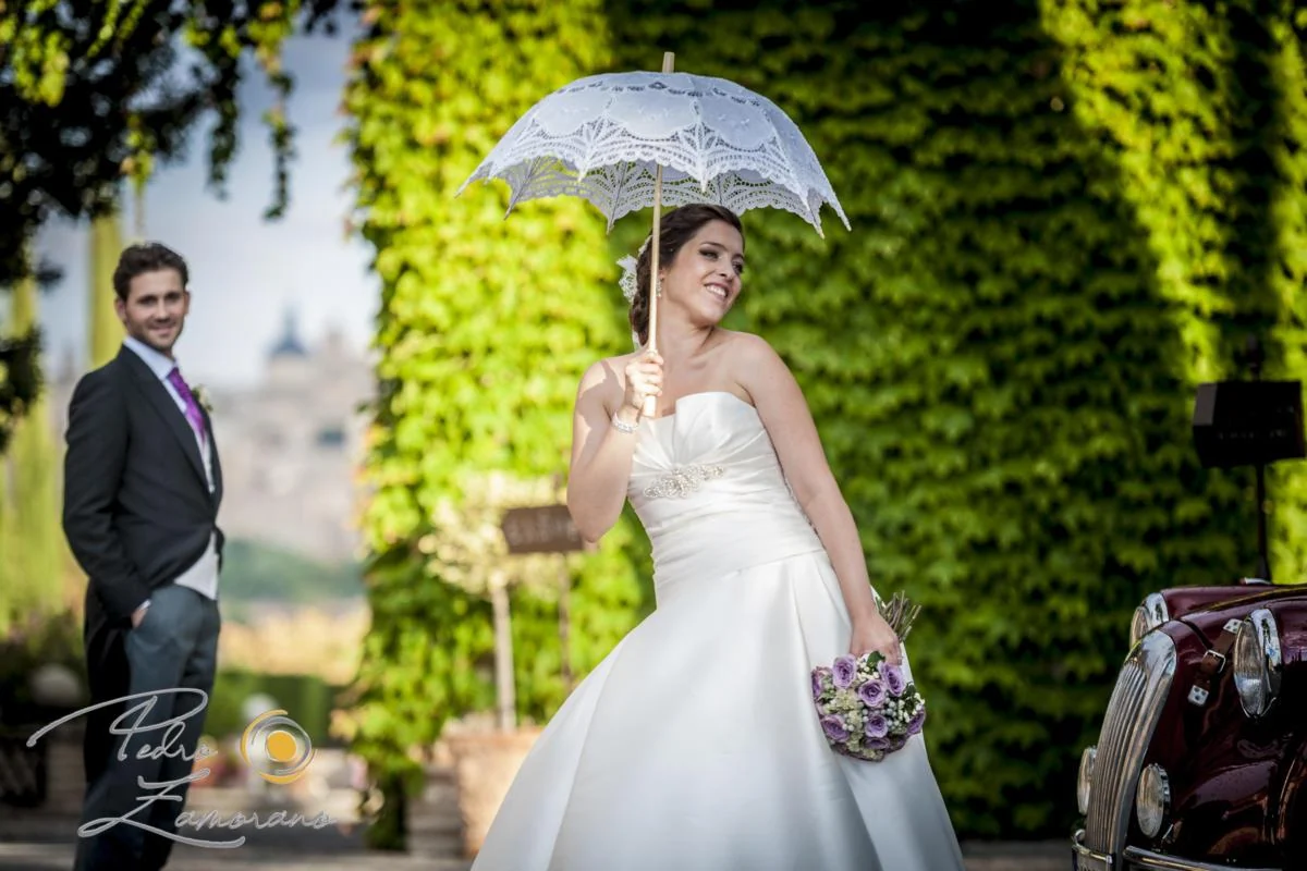 Novia con paraguas transparente en un jardín de hiedra del cigarral.