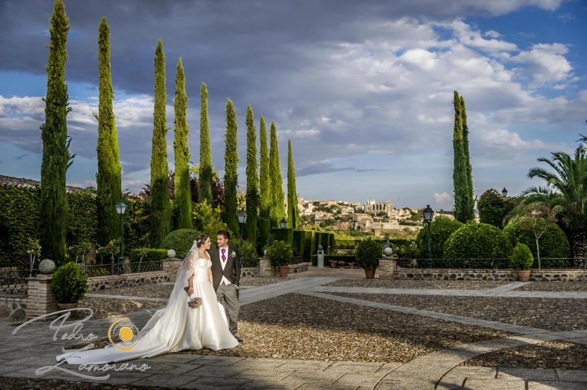 Novia en los jardines del Cigarral del Ángel Custodio con cipreses y Toledo al fondo.