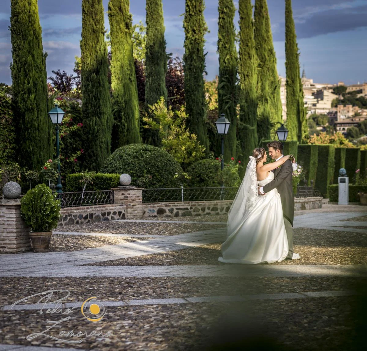 Novios abrazados en los jardines con cipreses del Cigarral del Ángel Custodio.
