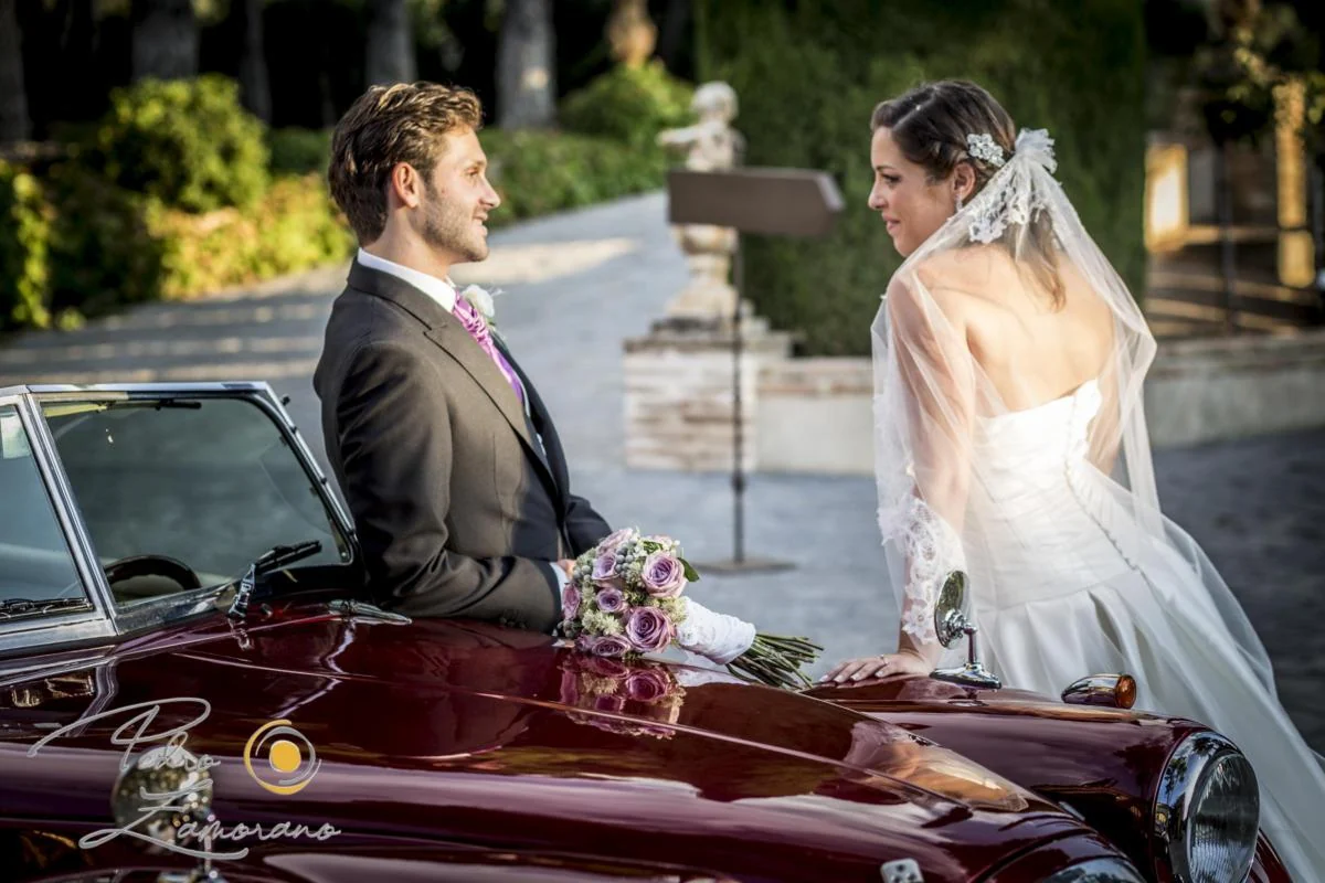 Novios junto a un coche clásico durante el reportaje de boda.