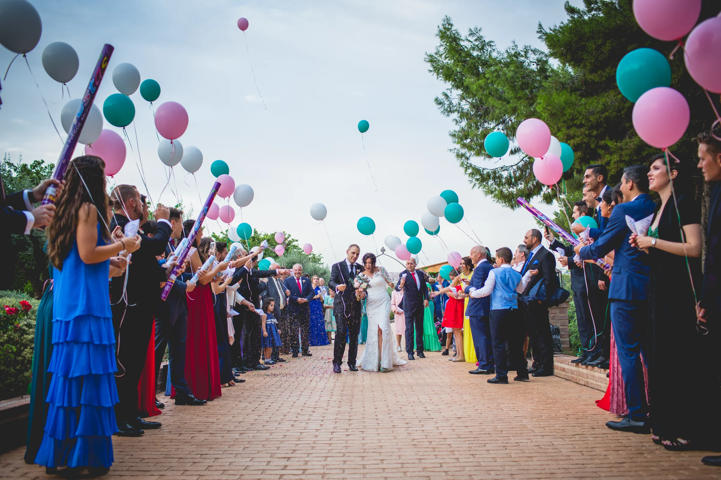Novios saliendo de la ceremonia entre invitados y globos de colores.