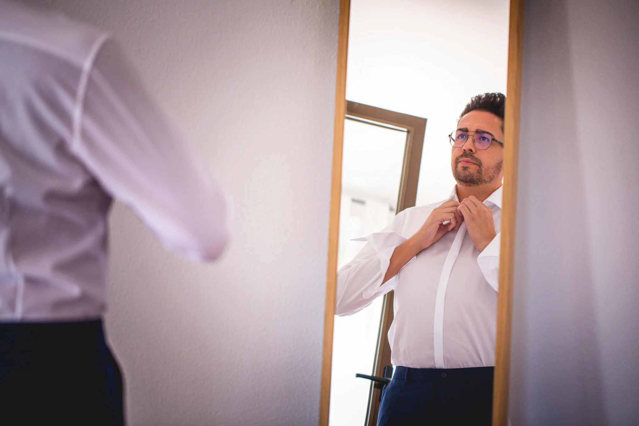 Novio abrochándose la camisa frente al espejo durante los preparativos de boda.