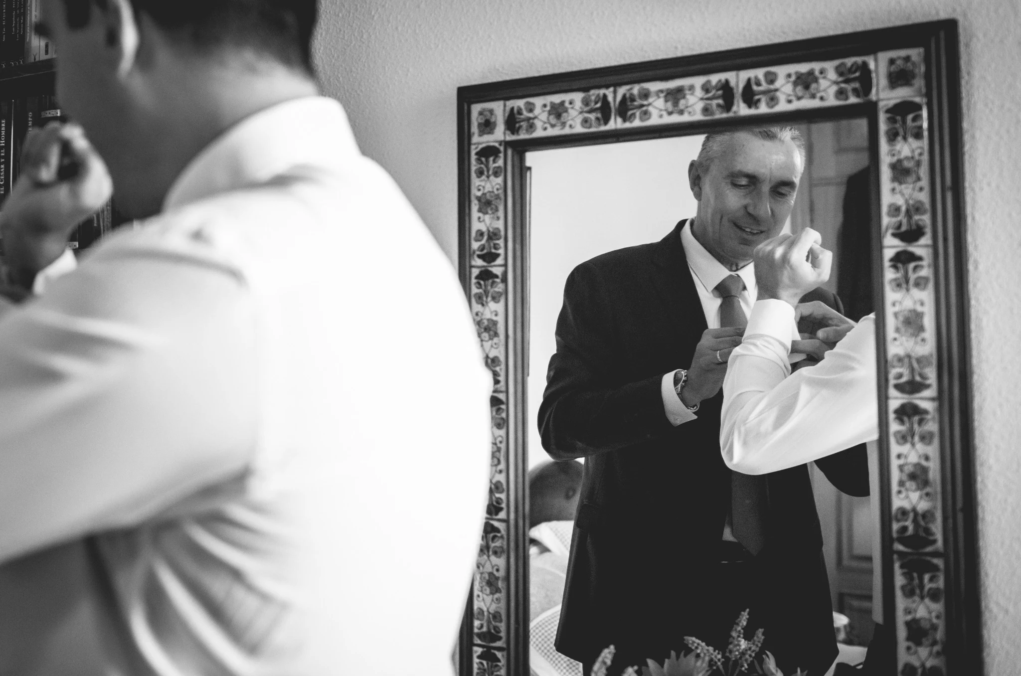 Padre del novio ayudándolo con la corbata reflejados en un espejo.