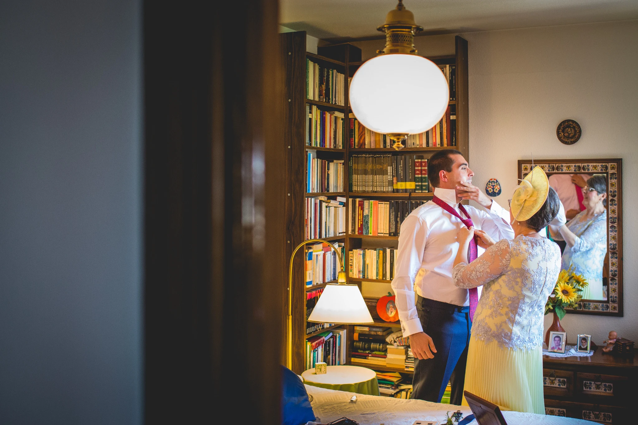 Madre del novio ajusta su corbata en una habitación familiar antes de la ceremonia.
