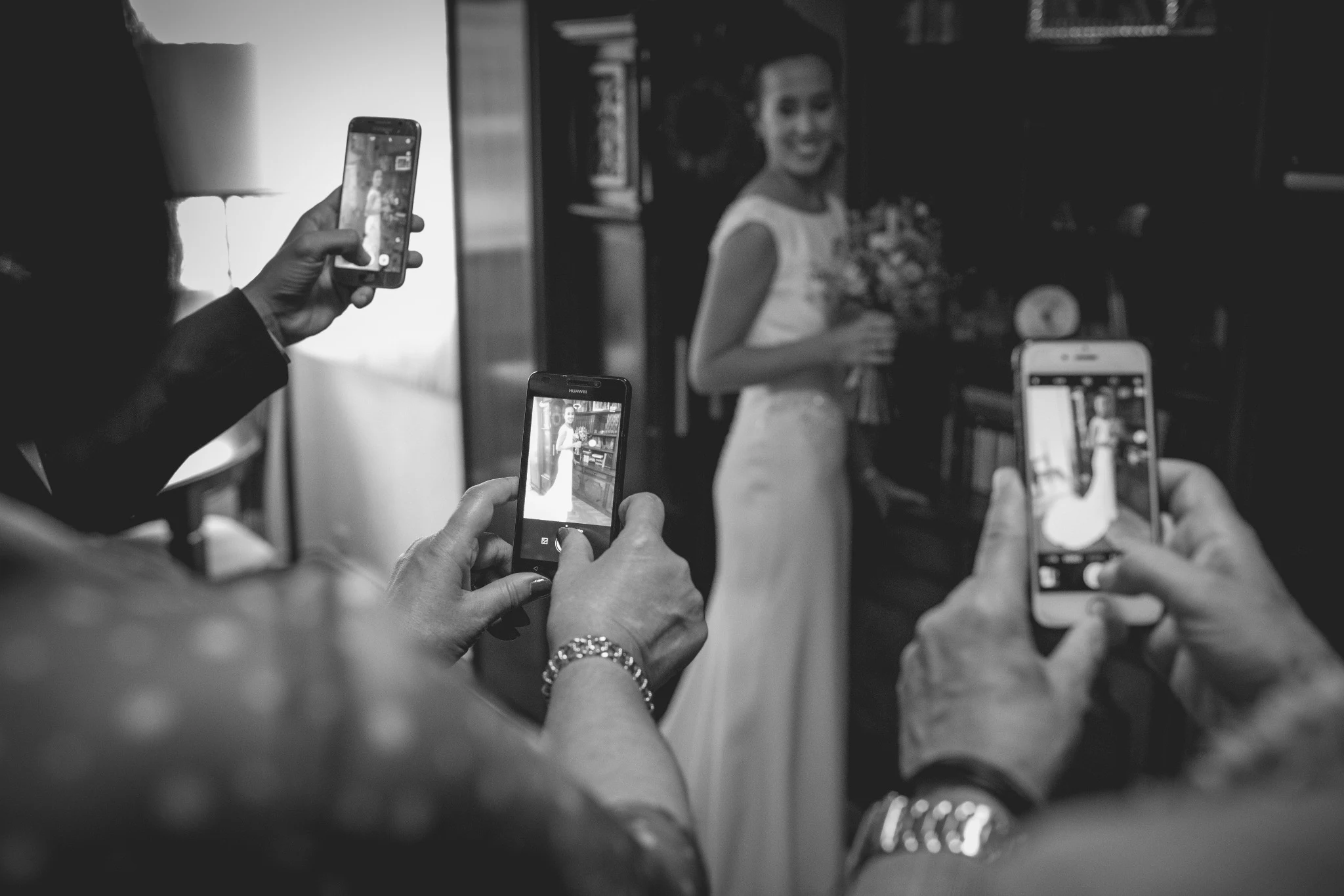 Varios invitados fotografían con sus teléfonos a la novia mientras sostiene el ramo.