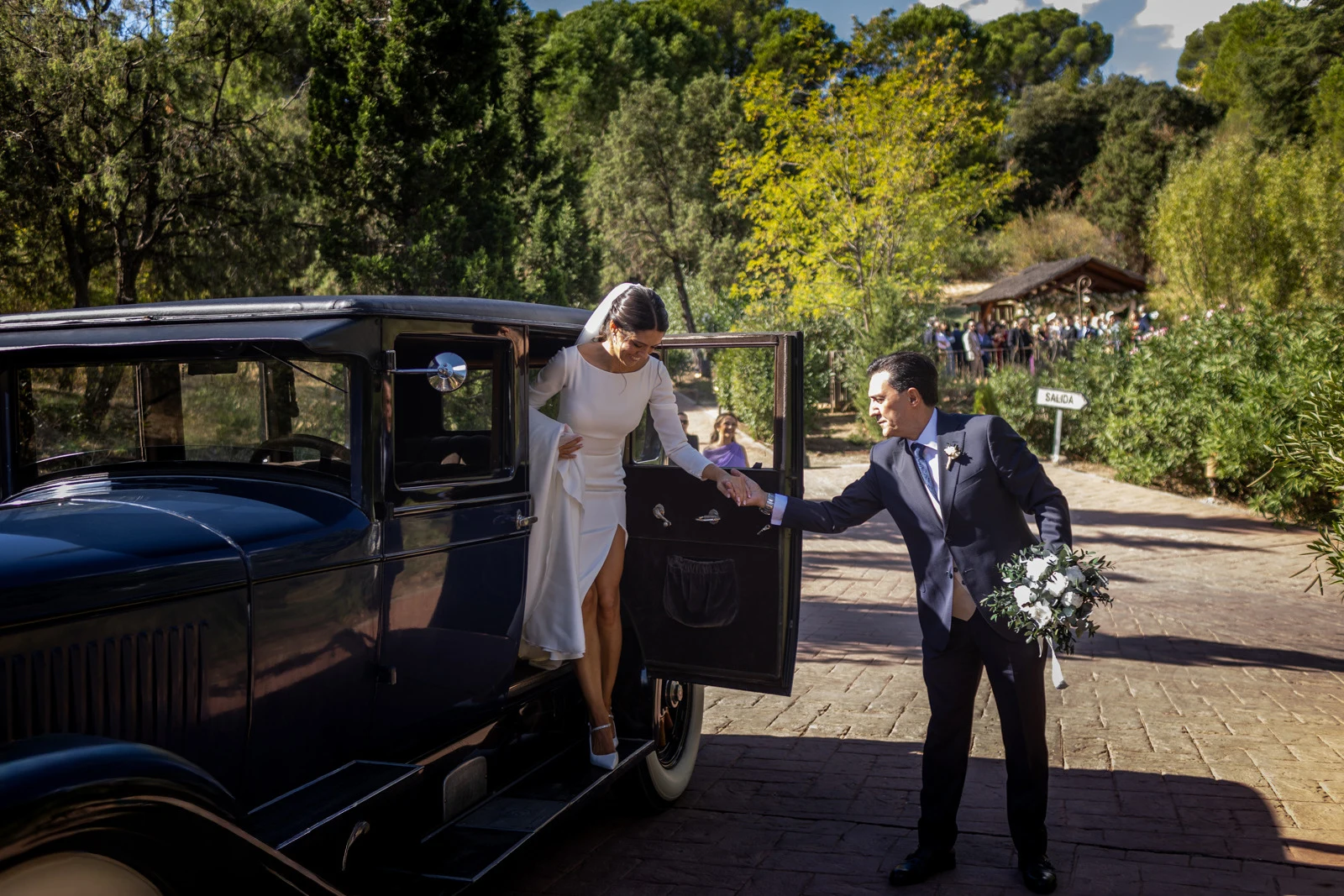 Novia bajando de un coche clásico ayudada por su acompañante a la llegada a la finca.