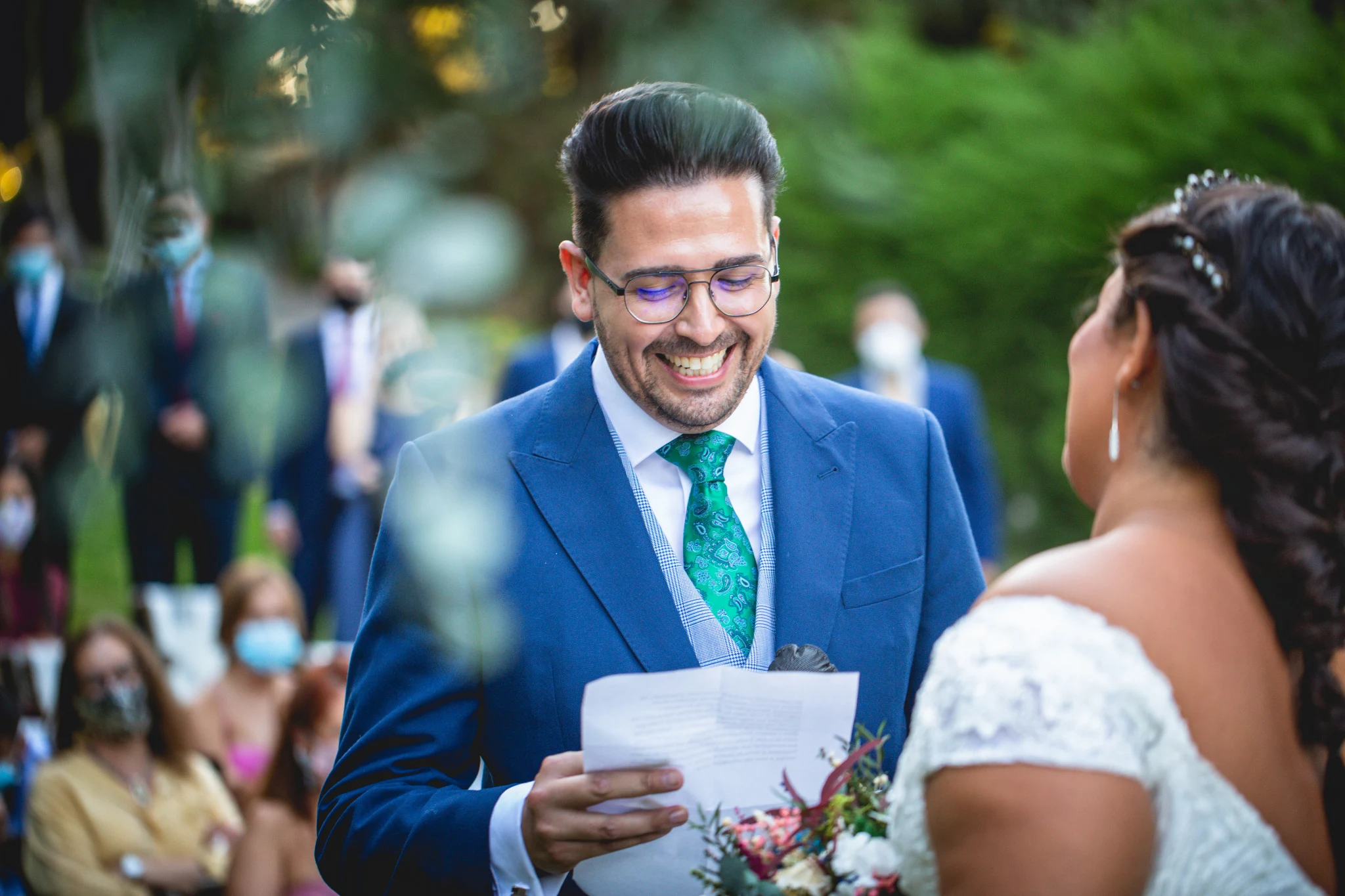 Novio sonríe mientras lee sus votos frente a la novia durante la ceremonia al aire libre.