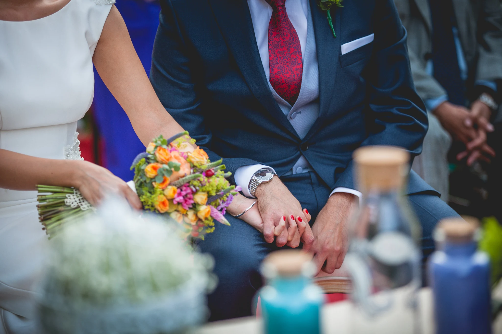 Detalle de las manos de los novios unidas durante la ceremonia junto al ramo de flores.