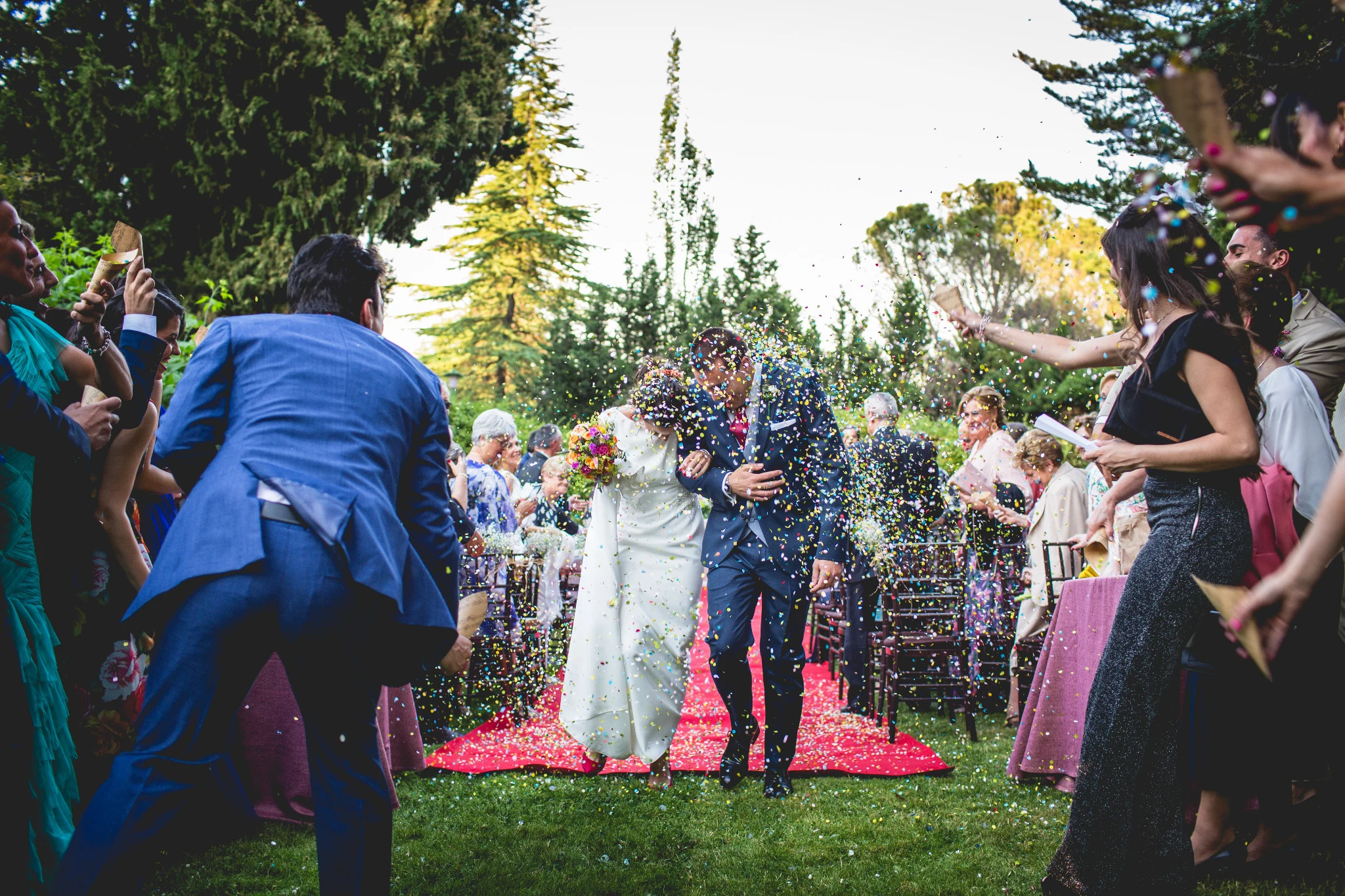 Novios avanzan entre los invitados mientras reciben una lluvia de confeti de colores.