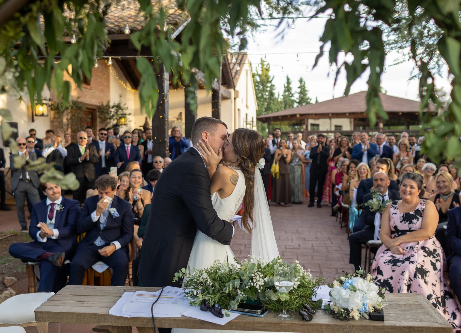 Novios se besan frente a todos los invitados al concluir una ceremonia al aire libre.