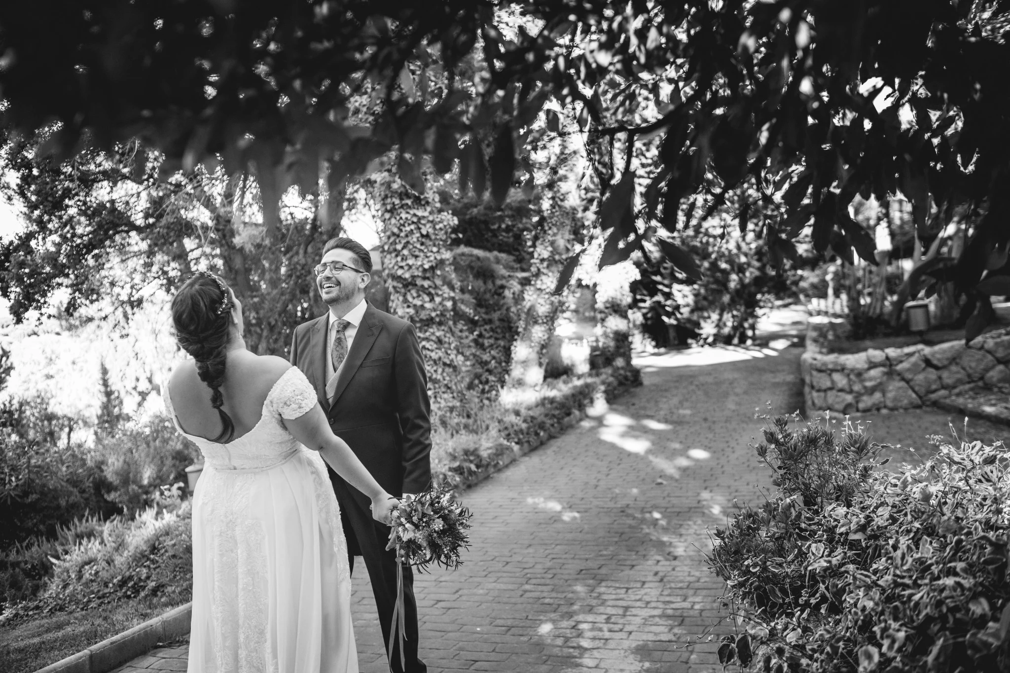 Novios caminando de la mano por un sendero rodeado de árboles en la finca.