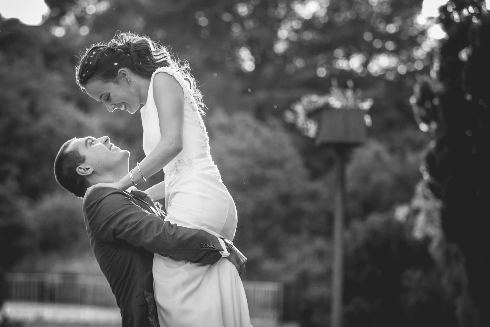 Novio levanta a la novia mientras ambos ríen en un retrato en blanco y negro.