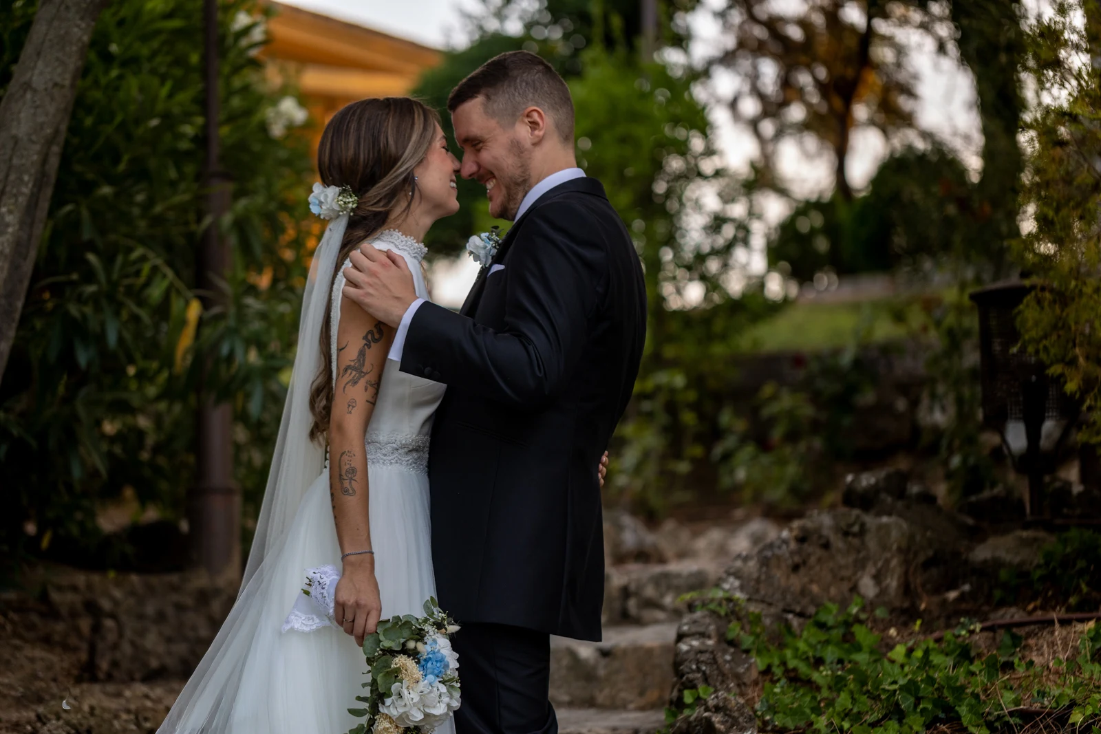 Novios cogidos de la mano se miran sonriendo con luz cálida de atardecer.
