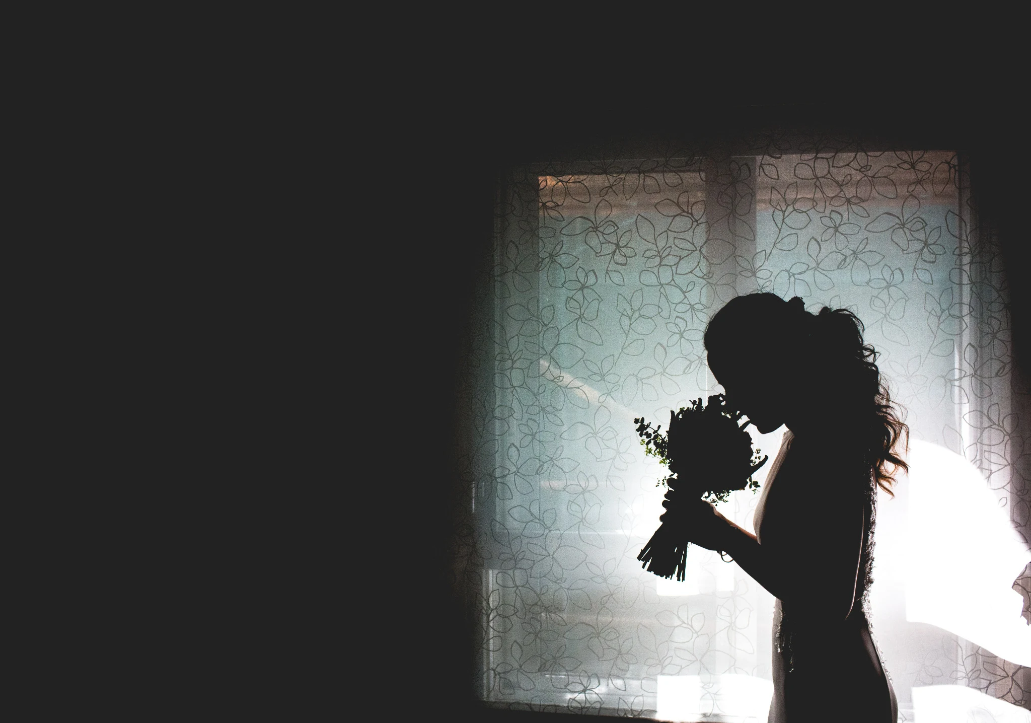 Silueta de una pareja de novios besándose frente a una ventana mientras la novia sostiene el ramo.
