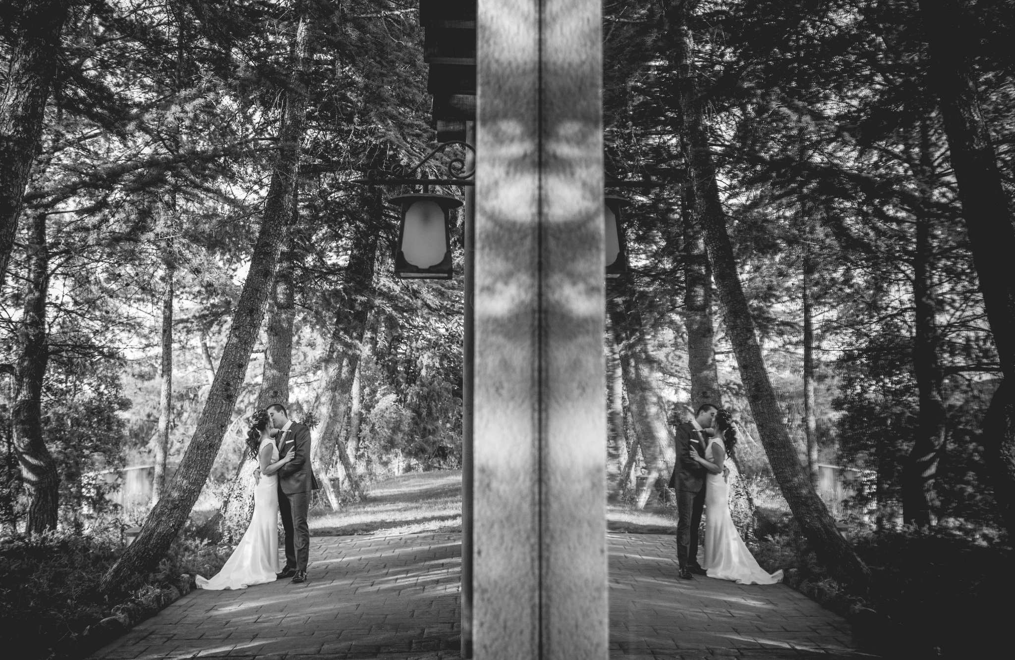Novios besándose en el bosque duplicados por el reflejo de un cristal en blanco y negro.