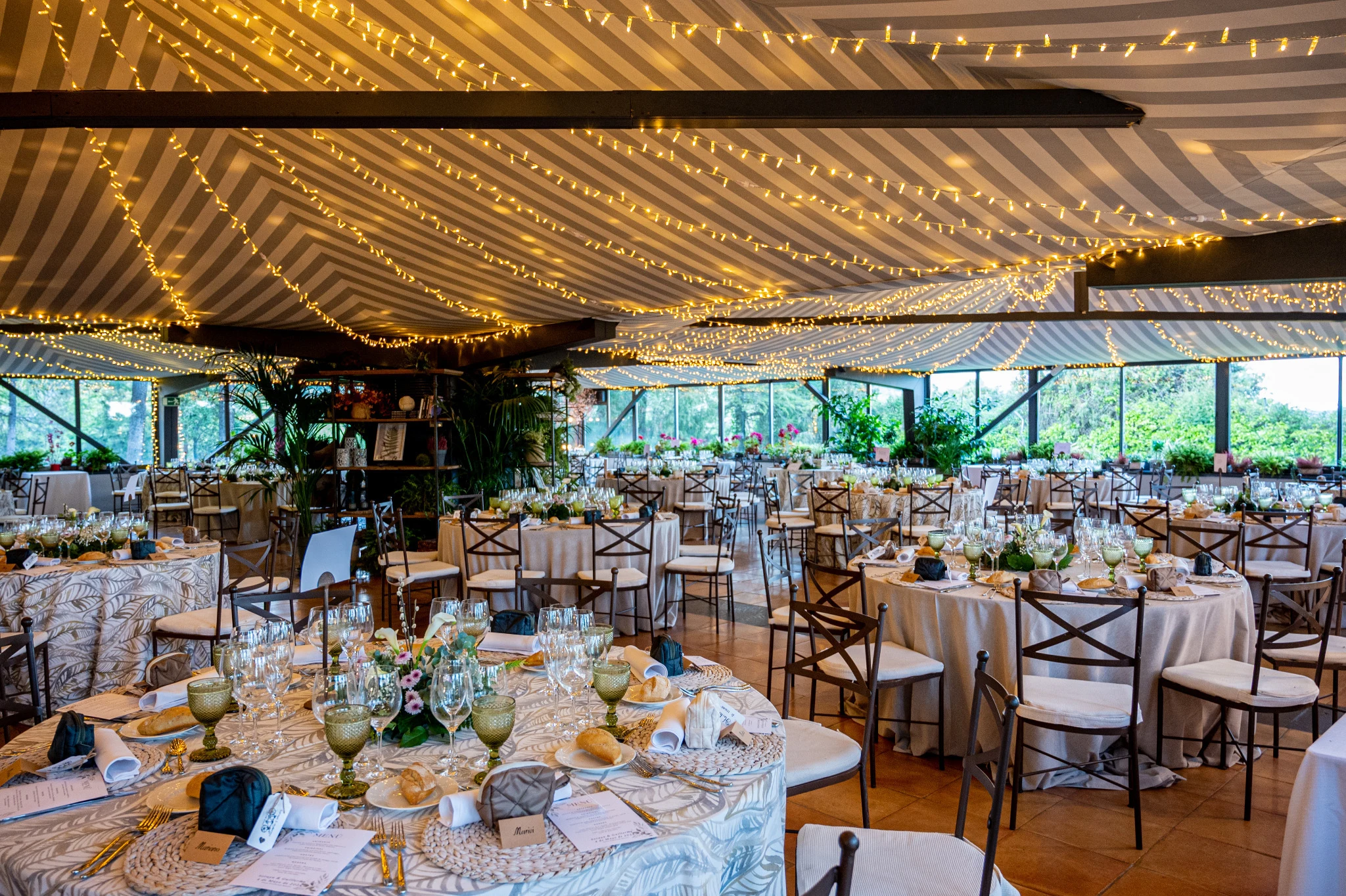 Salón preparado para el banquete con mesas redondas, copas y guirnaldas de luces.
