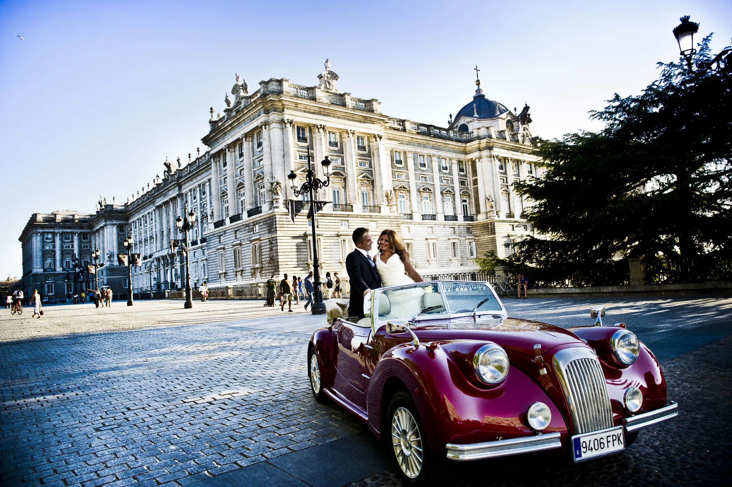 Una pareja de novios posa junto al Hurtan rojo cereza frente al Palacio Real de Madrid durante su reportaje de boda.