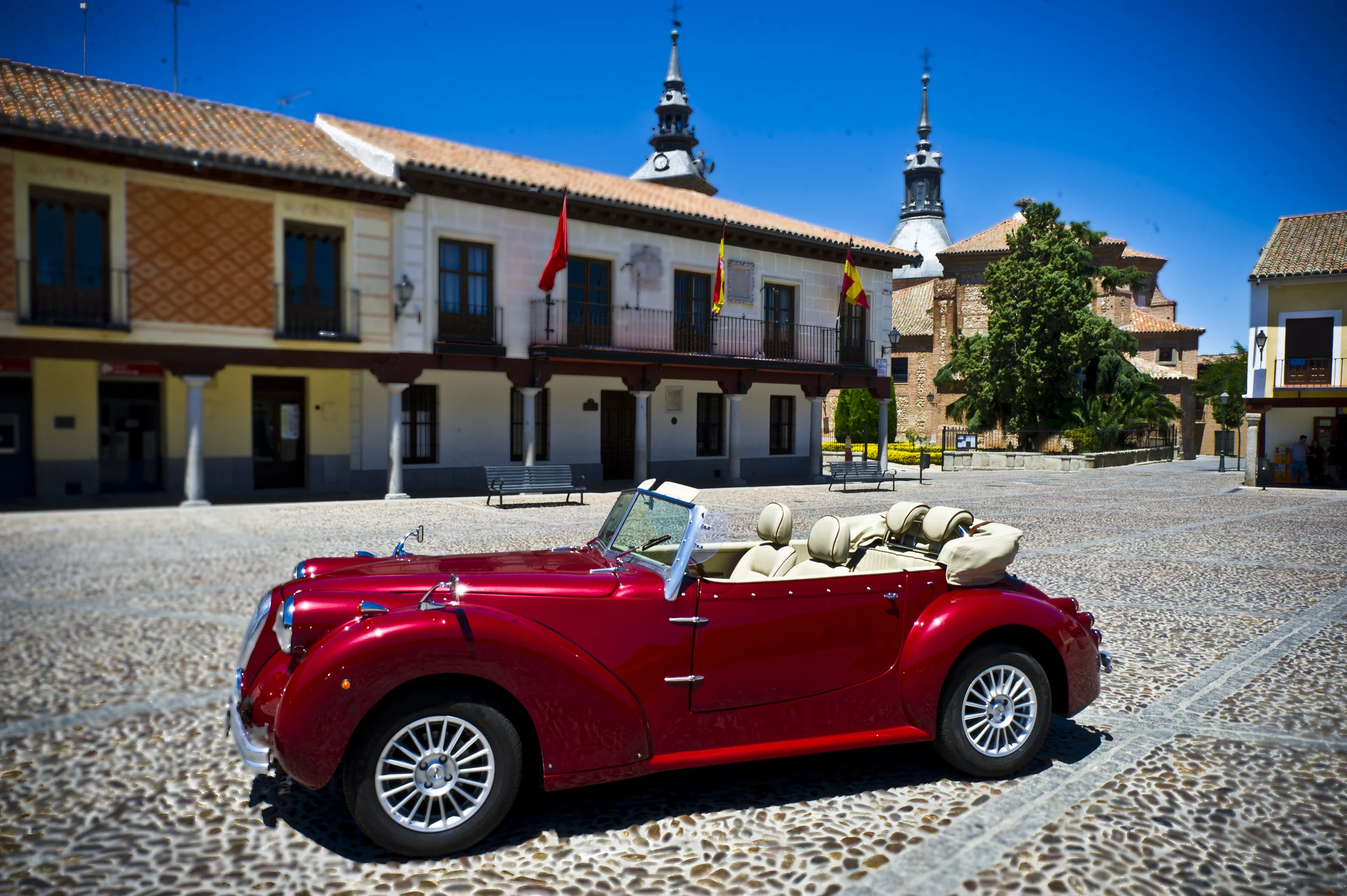 Hurtan rojo cereza descapotable estacionado de perfil en una plaza empedrada de ambiente histórico.