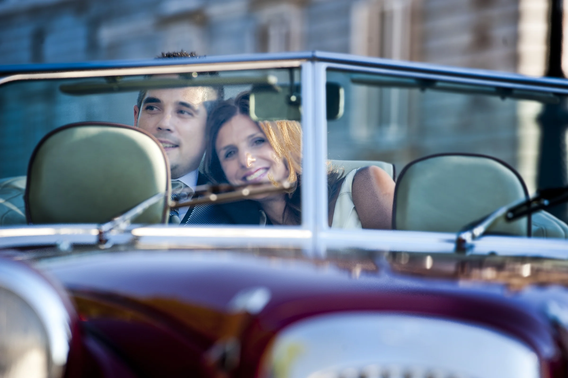 Una pareja de novios sonríe dentro del Hurtan descapotable, vista a través del parabrisas.