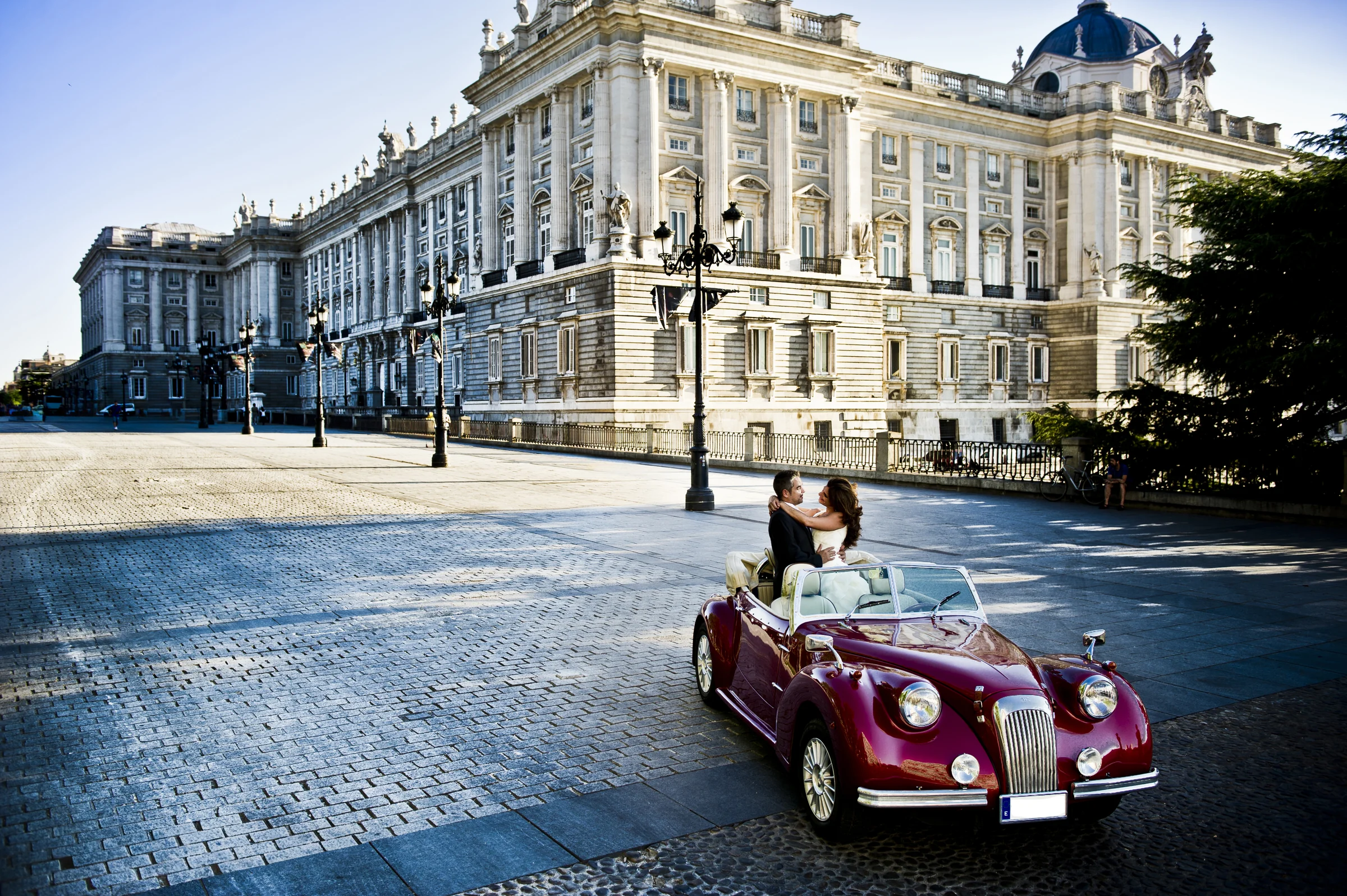 Una pareja de novios posa en el Hurtan rojo cereza en una amplia vista junto al Palacio Real de Madrid.