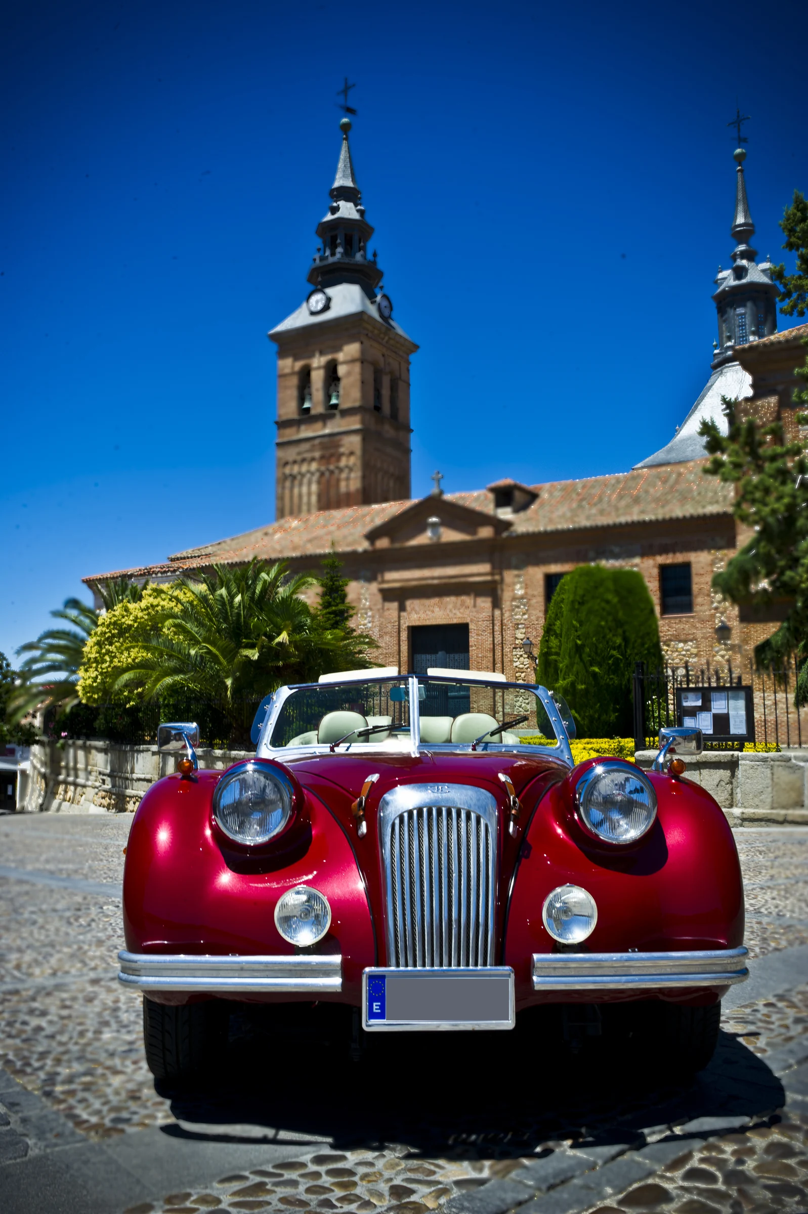 Vista frontal vertical del Hurtan rojo cereza ante una iglesia de ladrillo en una plaza histórica.