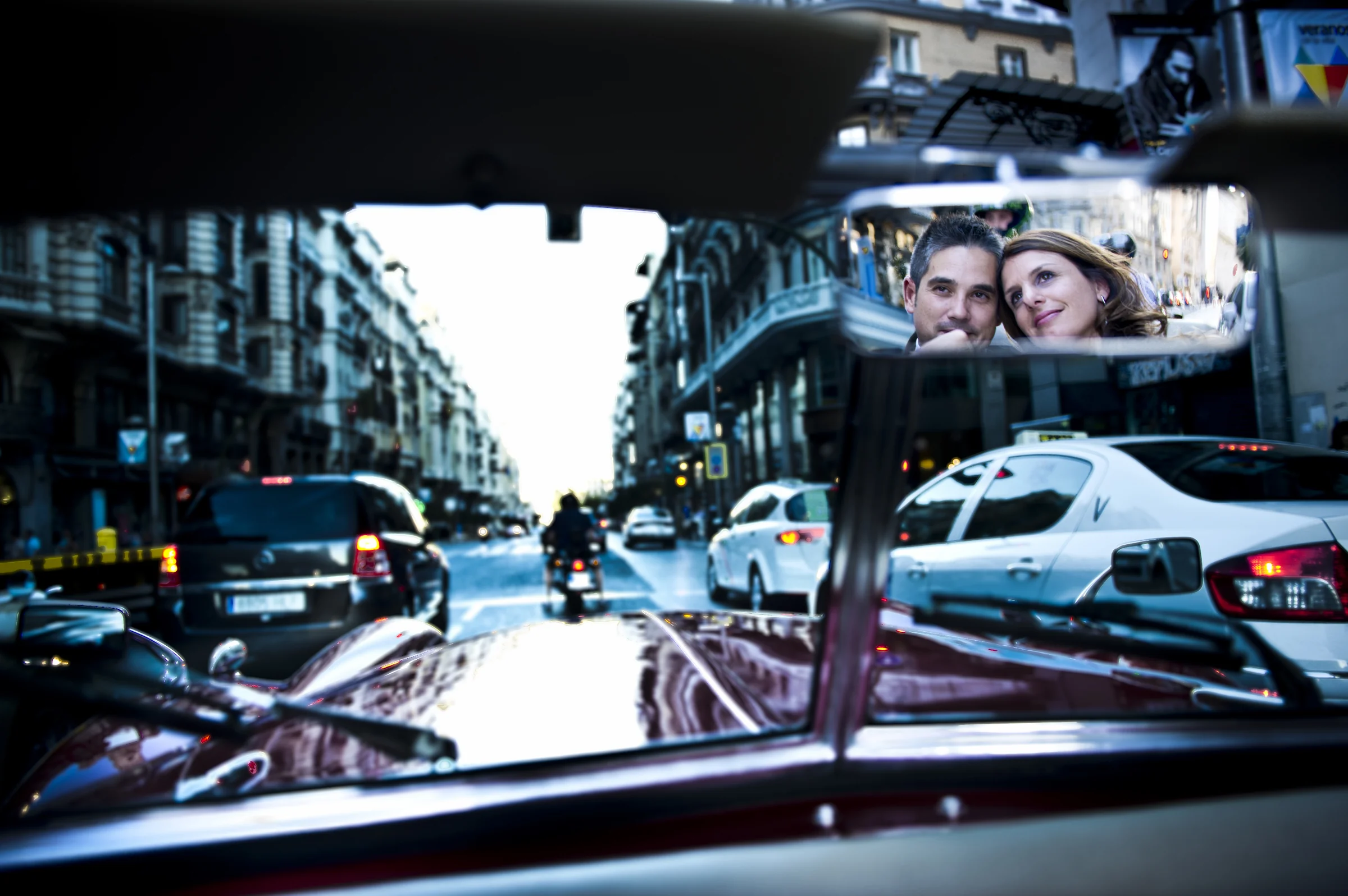 Los novios se reflejan juntos en el retrovisor del Hurtan mientras el coche circula por una calle de Madrid.