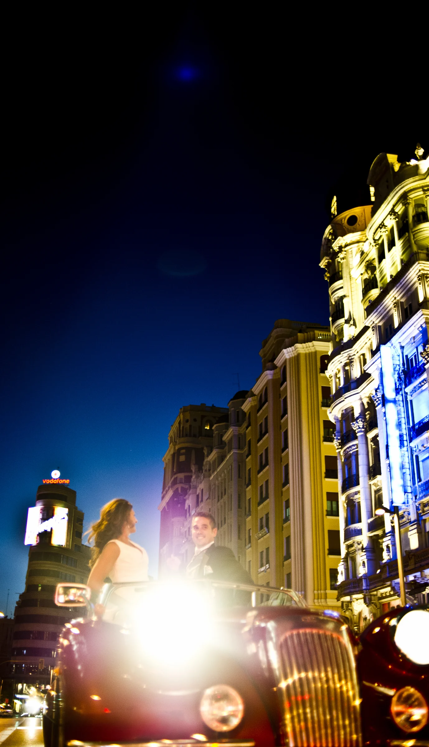 Los novios posan en el Hurtan rojo cereza con los faros encendidos entre las luces nocturnas del centro de Madrid.
