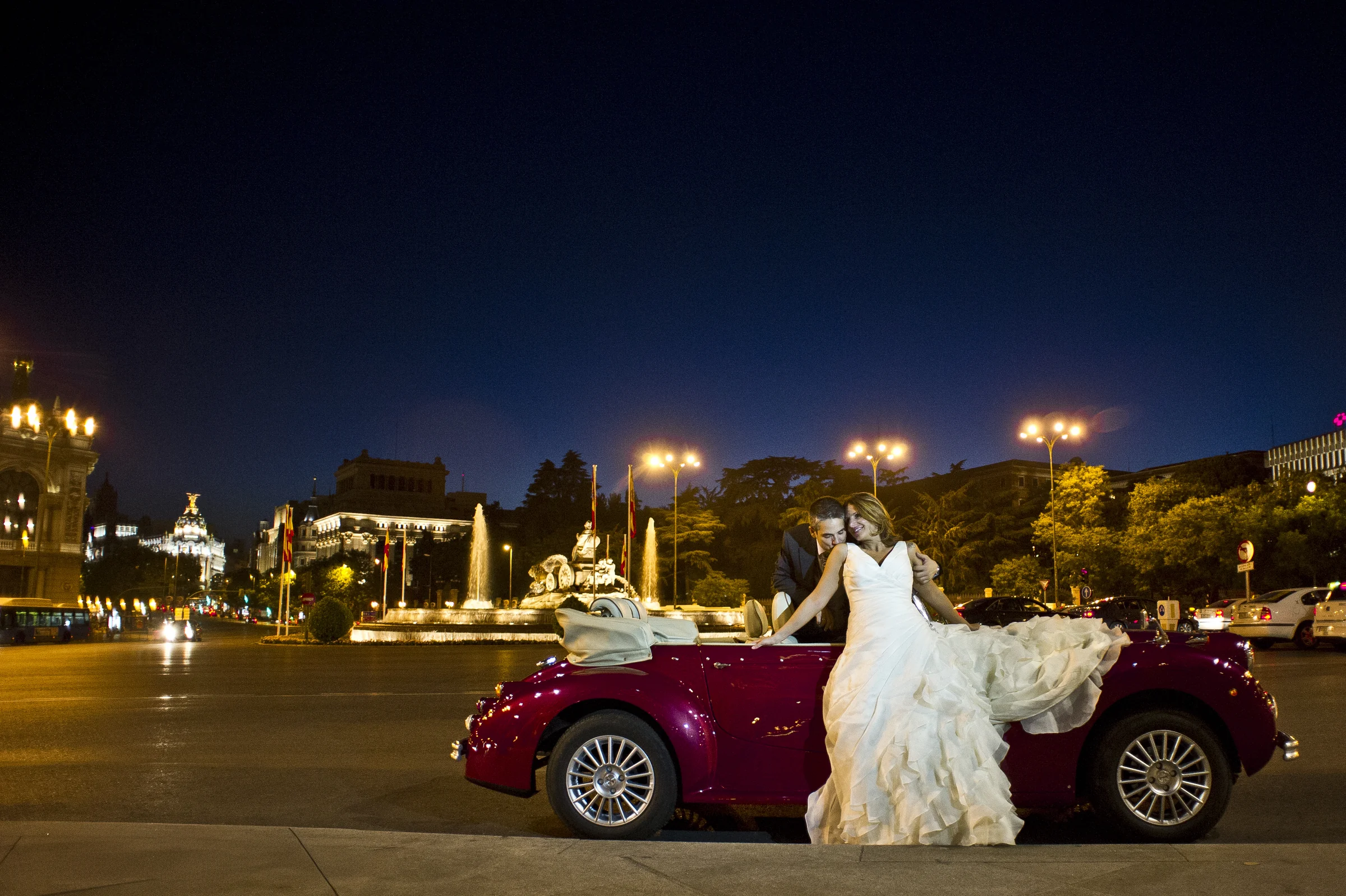 Una pareja de novios posa junto al Hurtan rojo cereza de noche en la plaza de Cibeles de Madrid.