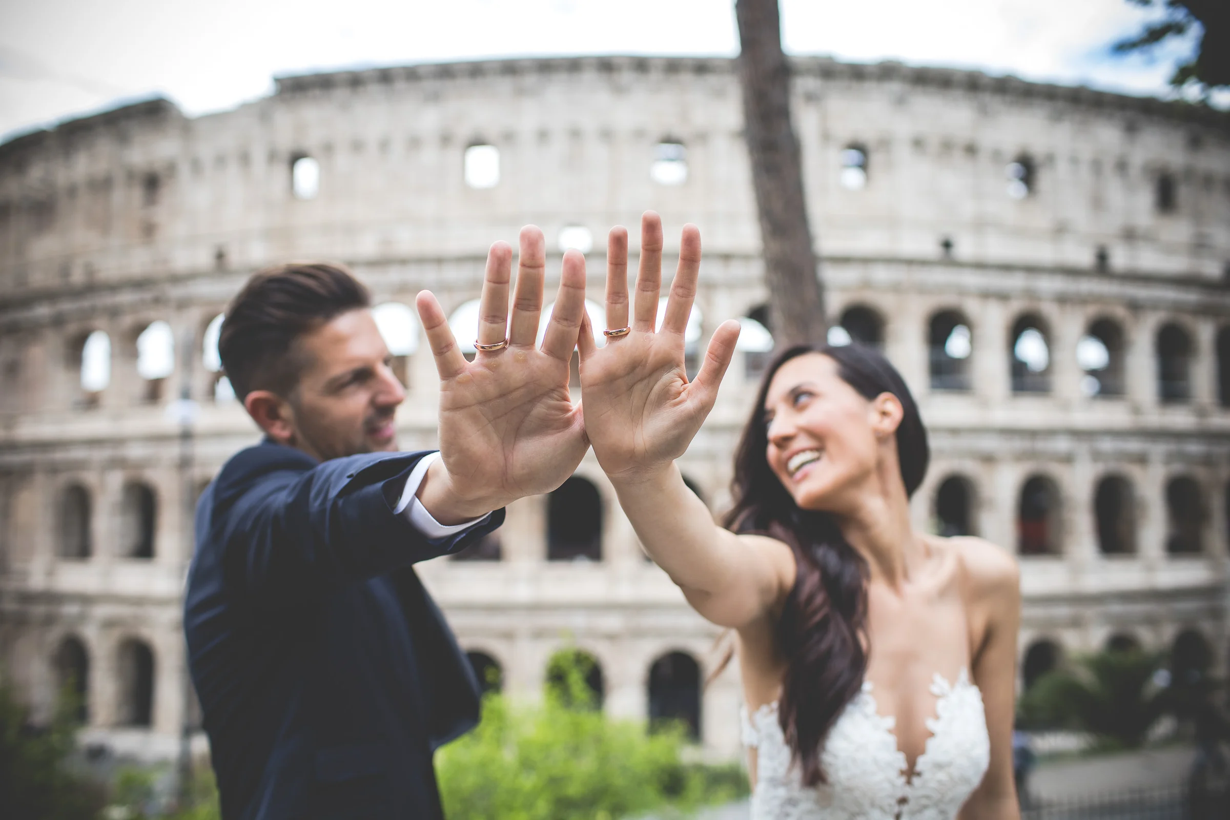 Los novios juegan levantando las manos delante del Coliseo durante una sesión postboda en Coliseo de Roma.