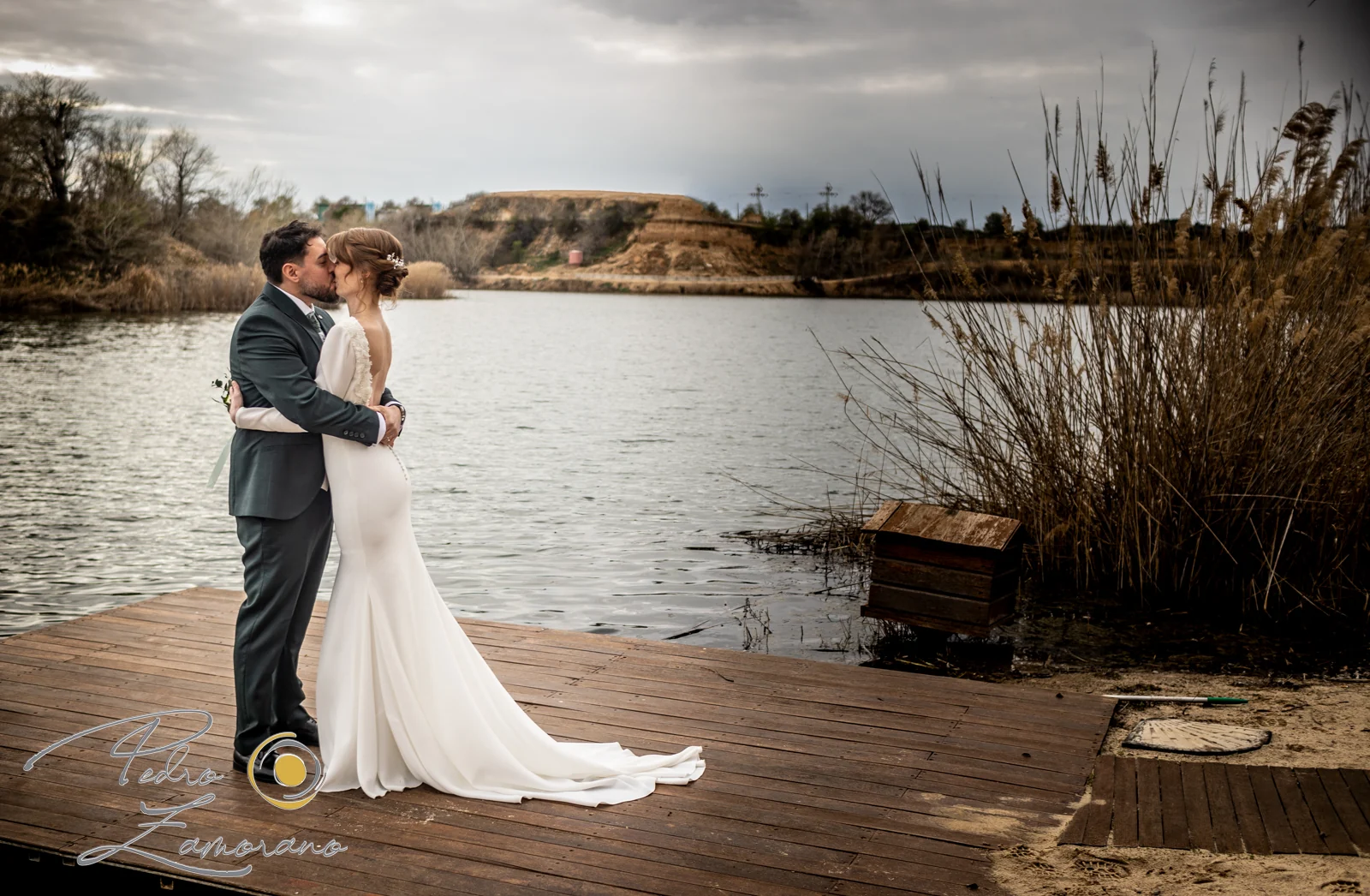 Novios junto al lago en una pasarela de madera en una boda en Complejo La Cigüeña