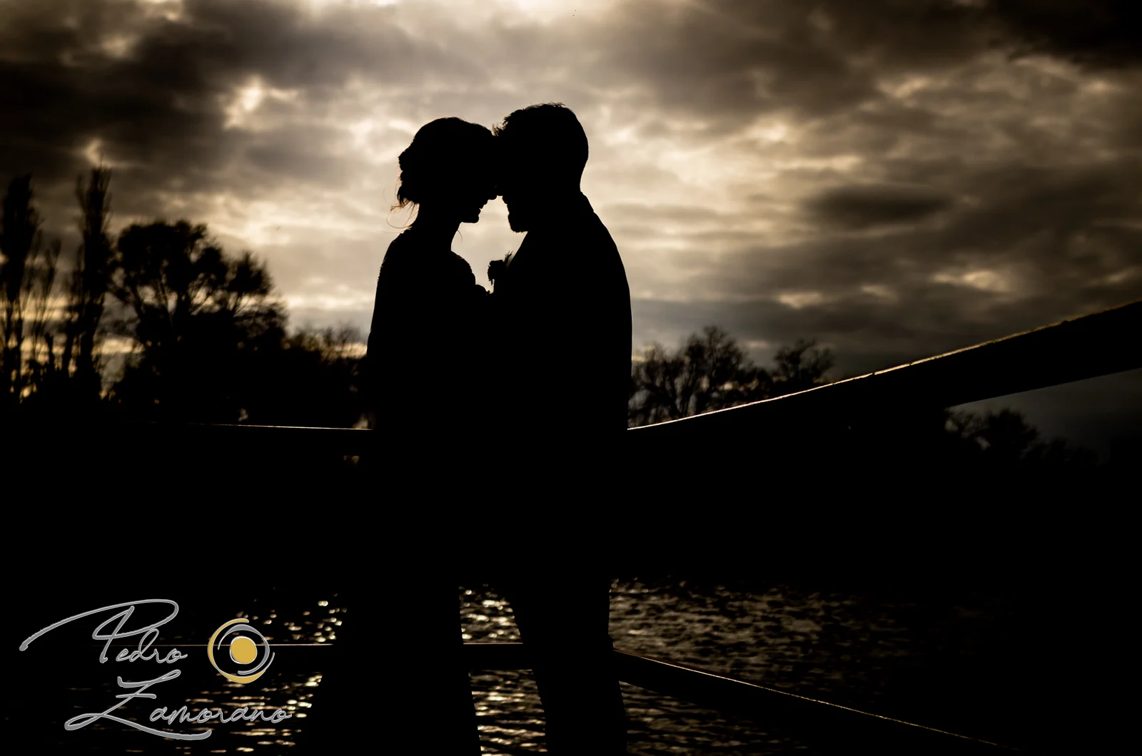 Silueta de los novios al atardecer junto al lago en una boda en Complejo La Cigüeña
