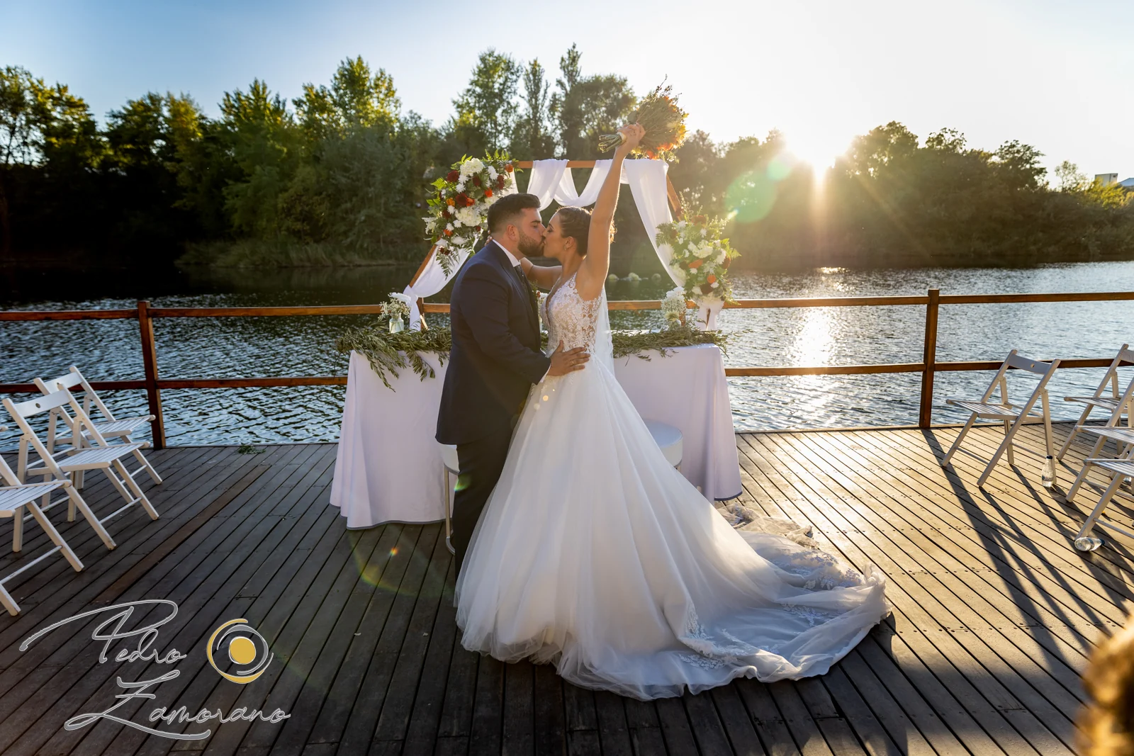 Novios besándose junto al lago durante la ceremonia en una boda en Complejo La Cigüeña