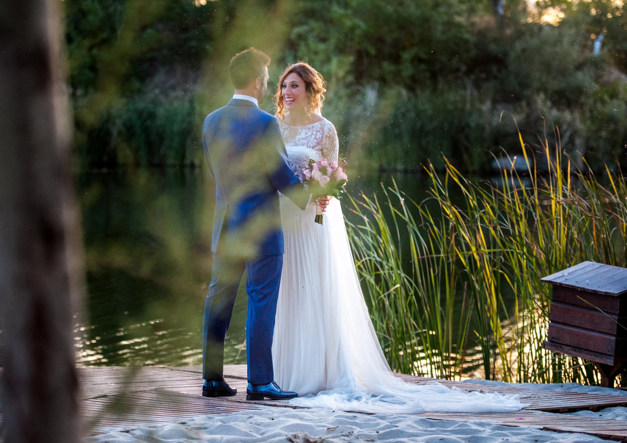 Novios abrazados junto a la vegetación del lago en una boda en Complejo La Cigüeña