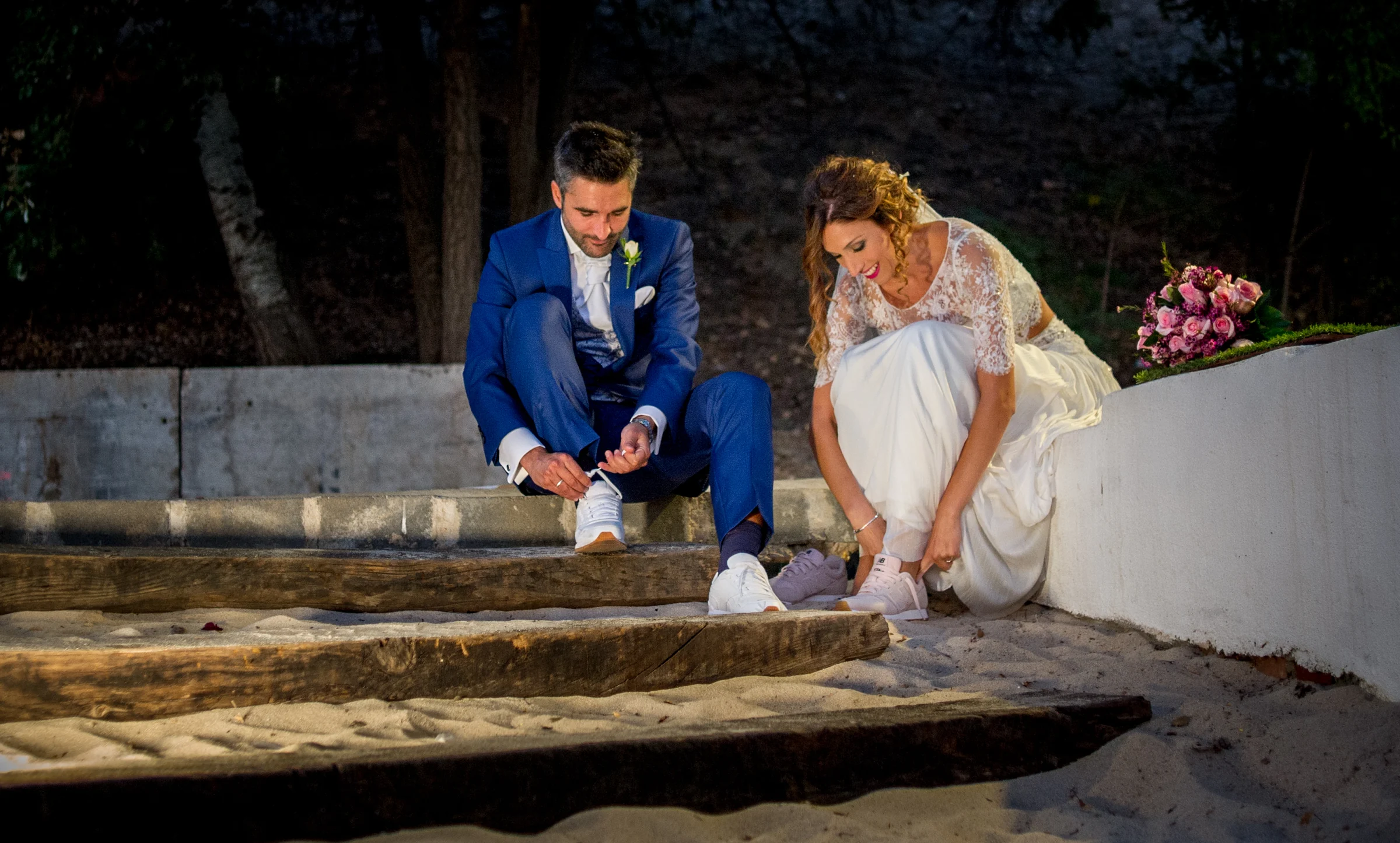 Novios sentados en un muro junto al agua en una boda en Complejo La Cigüeña
