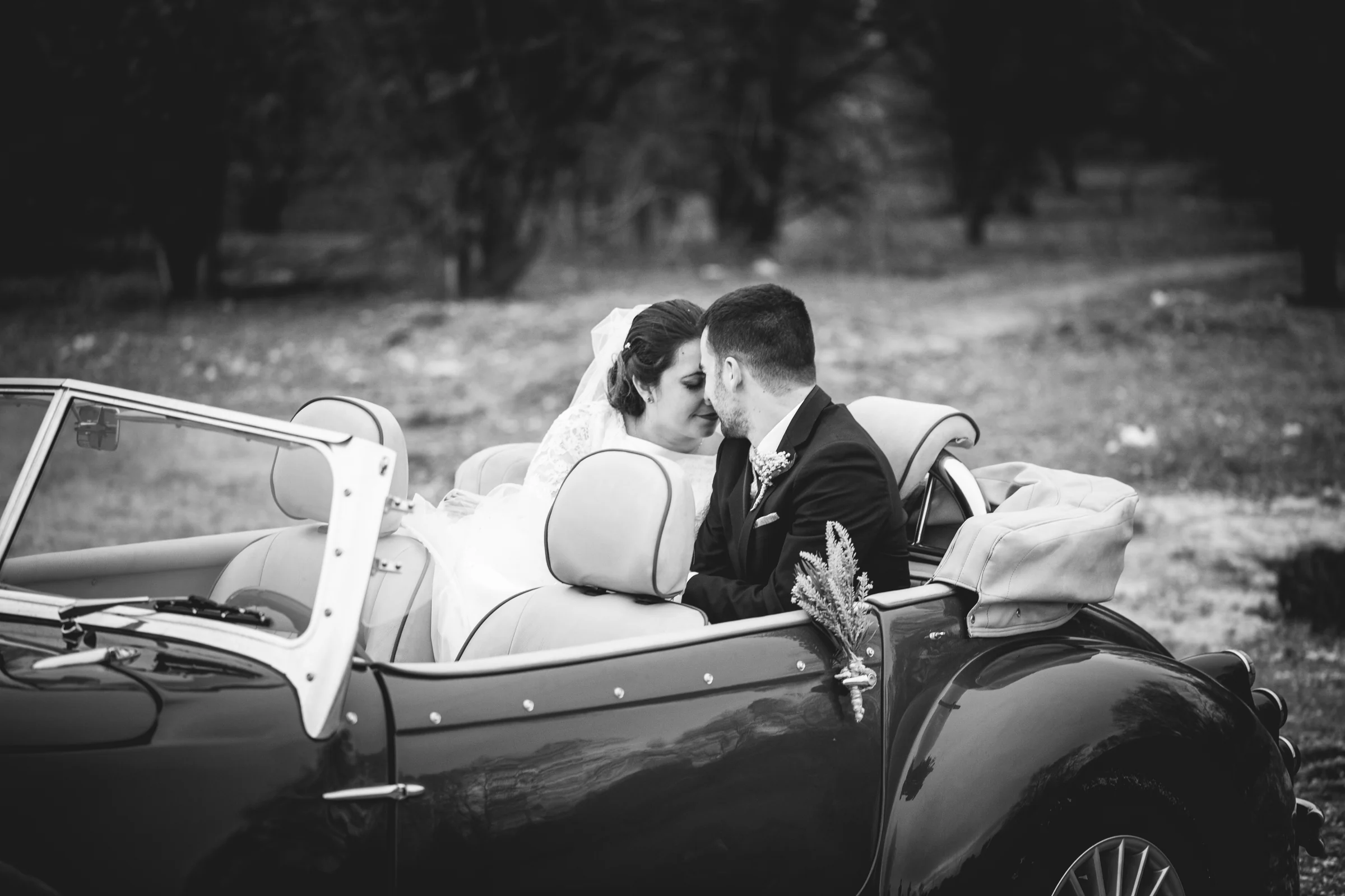Novios en coche clásico descapotable en blanco y negro en una boda en Complejo La Cigüeña