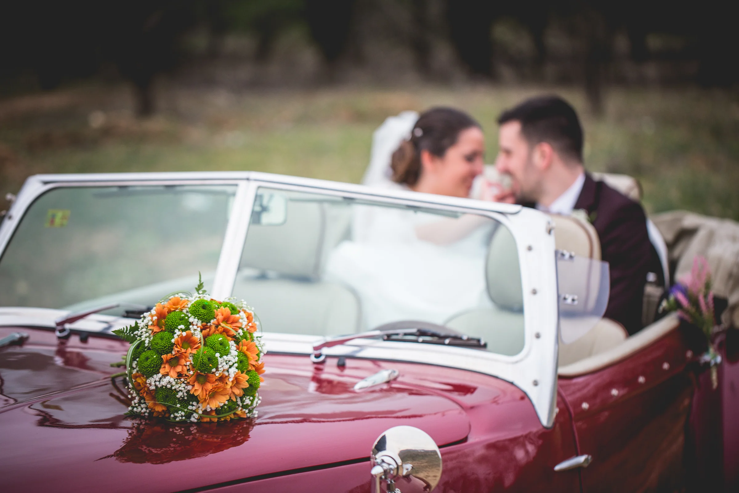 Novios junto a coche clásico rojo en una boda en Complejo La Cigüeña