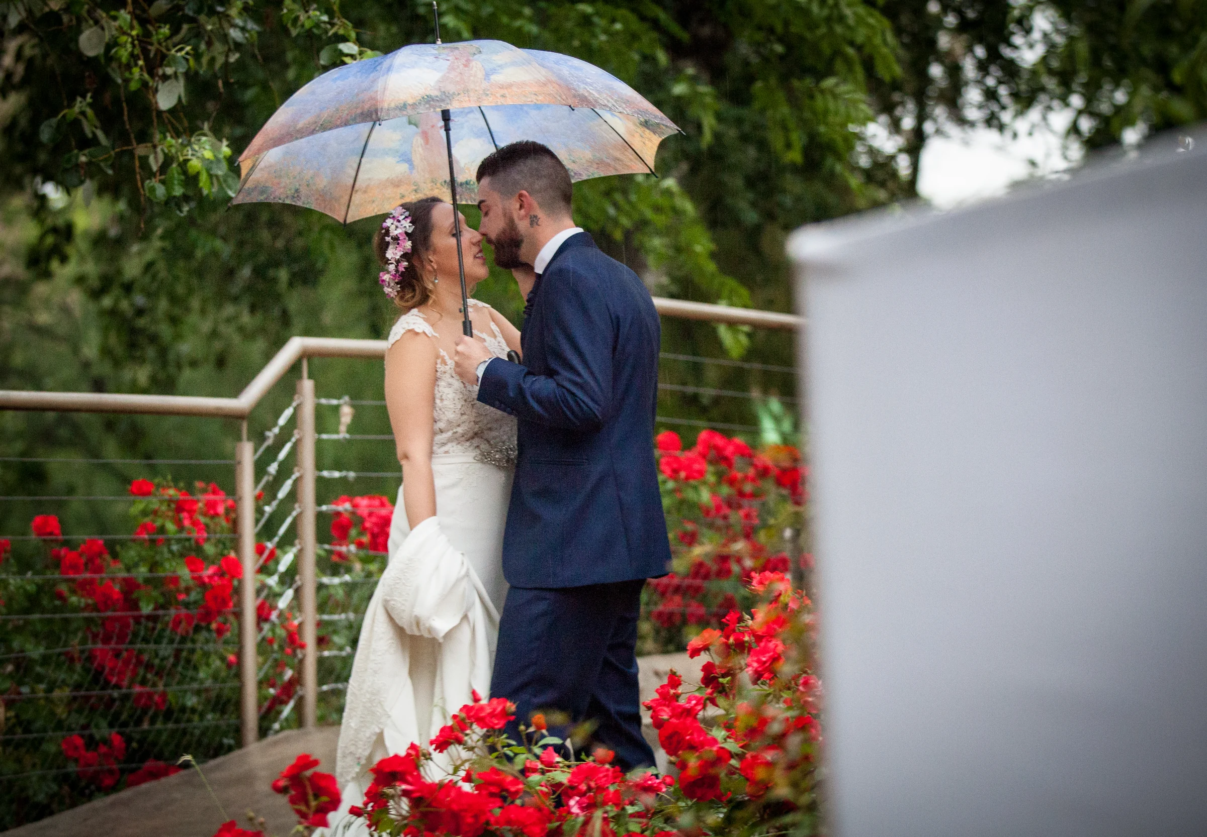 Novios bajo paraguas junto a flores en una boda en Complejo La Cigüeña