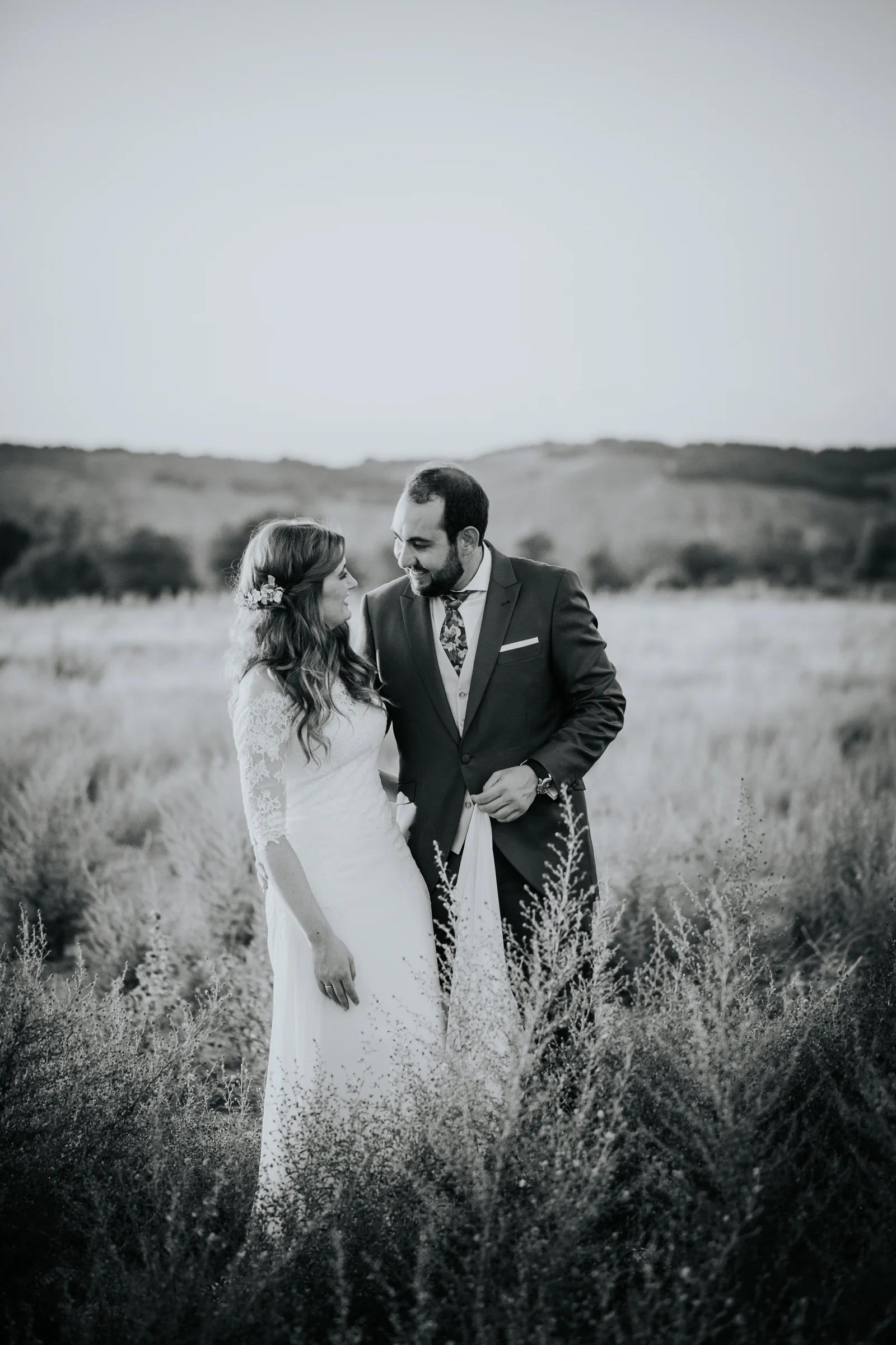 Novios caminando por el campo en blanco y negro en una boda en Complejo La Cigüeña