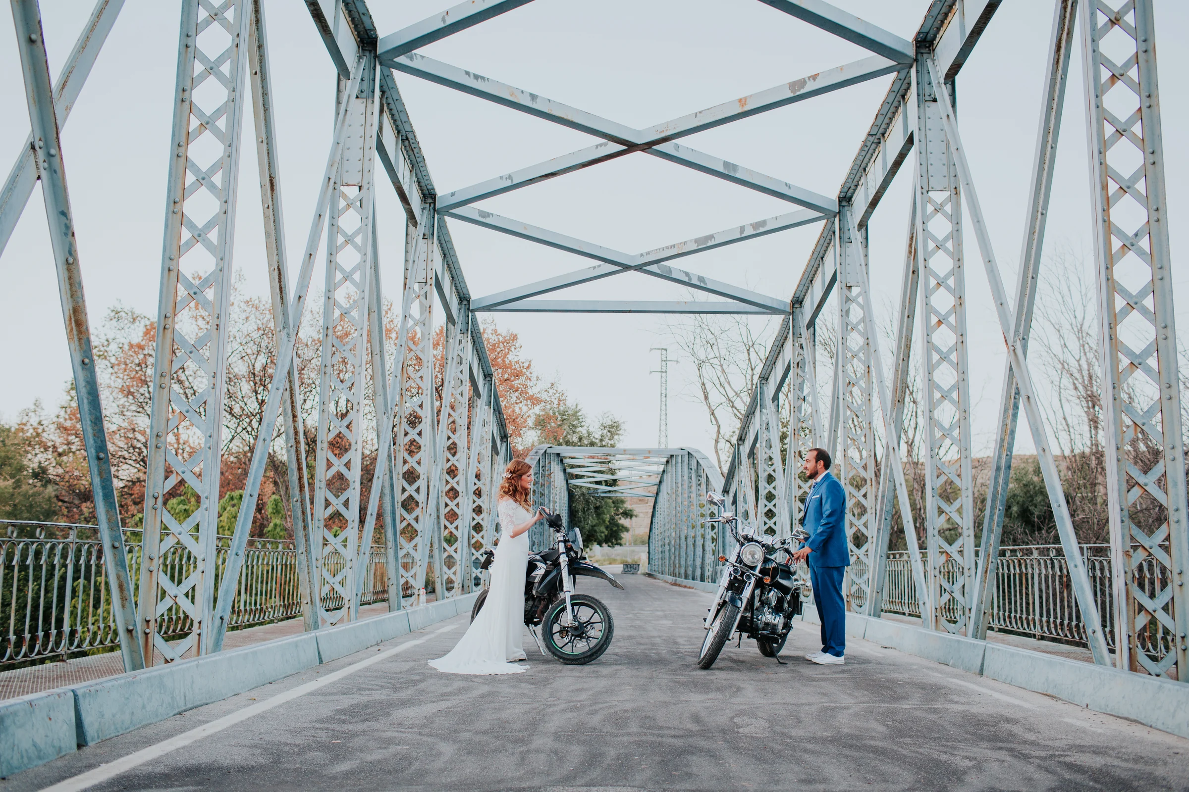 Novios en un puente metálico con motocicleta en una boda en Complejo La Cigüeña