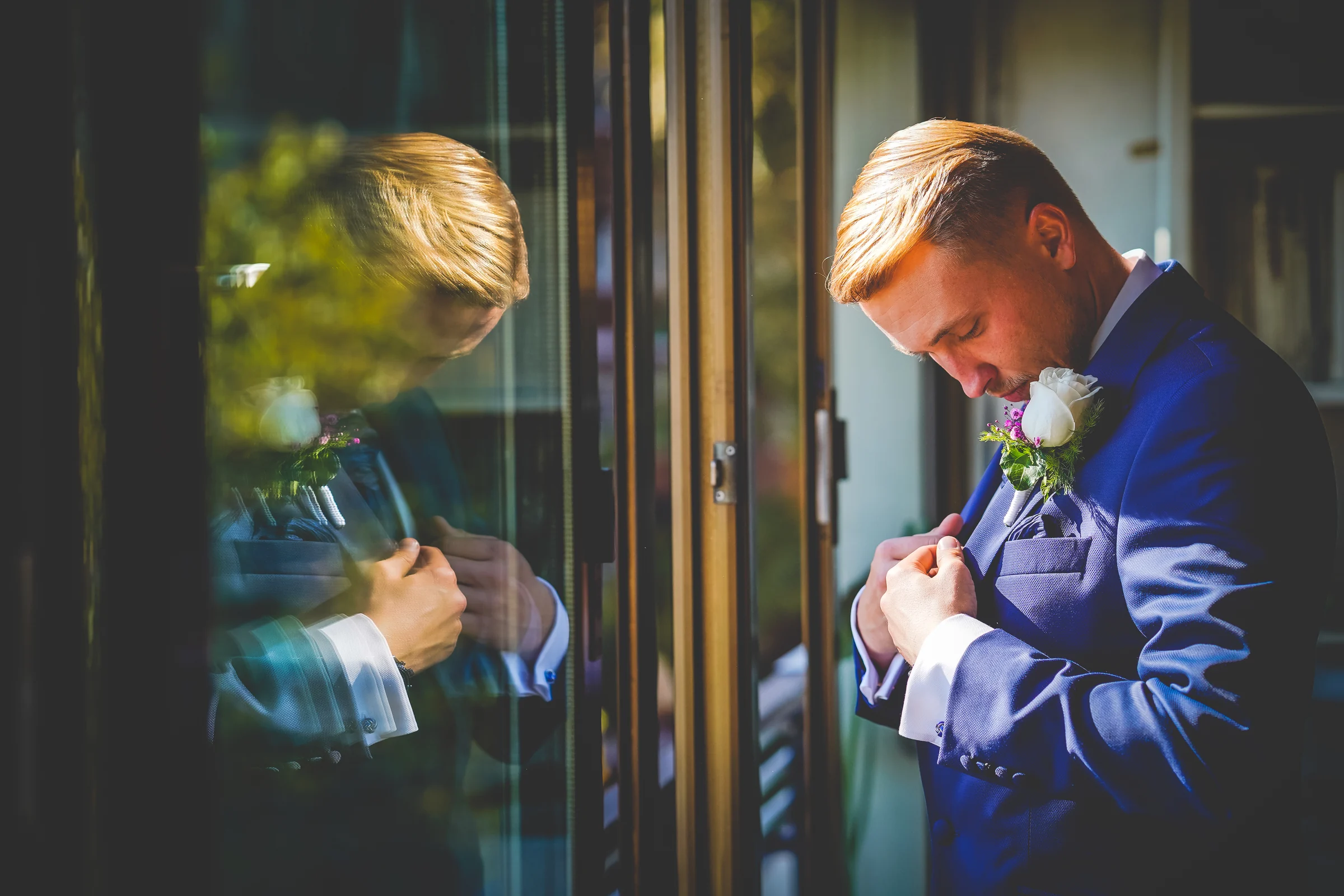 Novio ajustando la chaqueta junto a cristal durante una boda en Mirador de Cuatro Vientos.