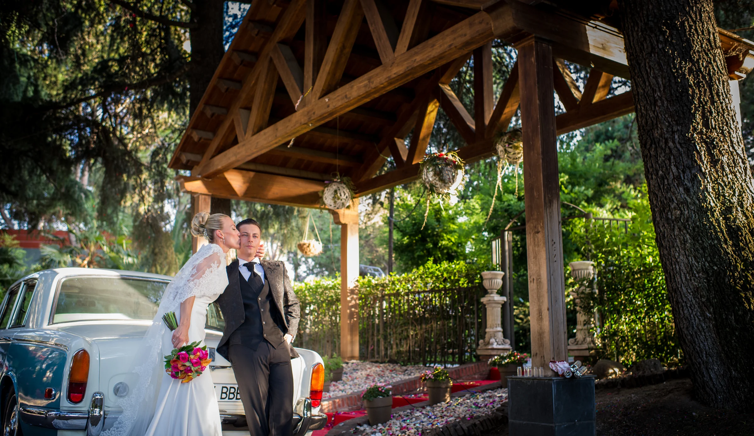 Novios junto al coche bajo pergola durante una boda en Mirador de Cuatro Vientos.