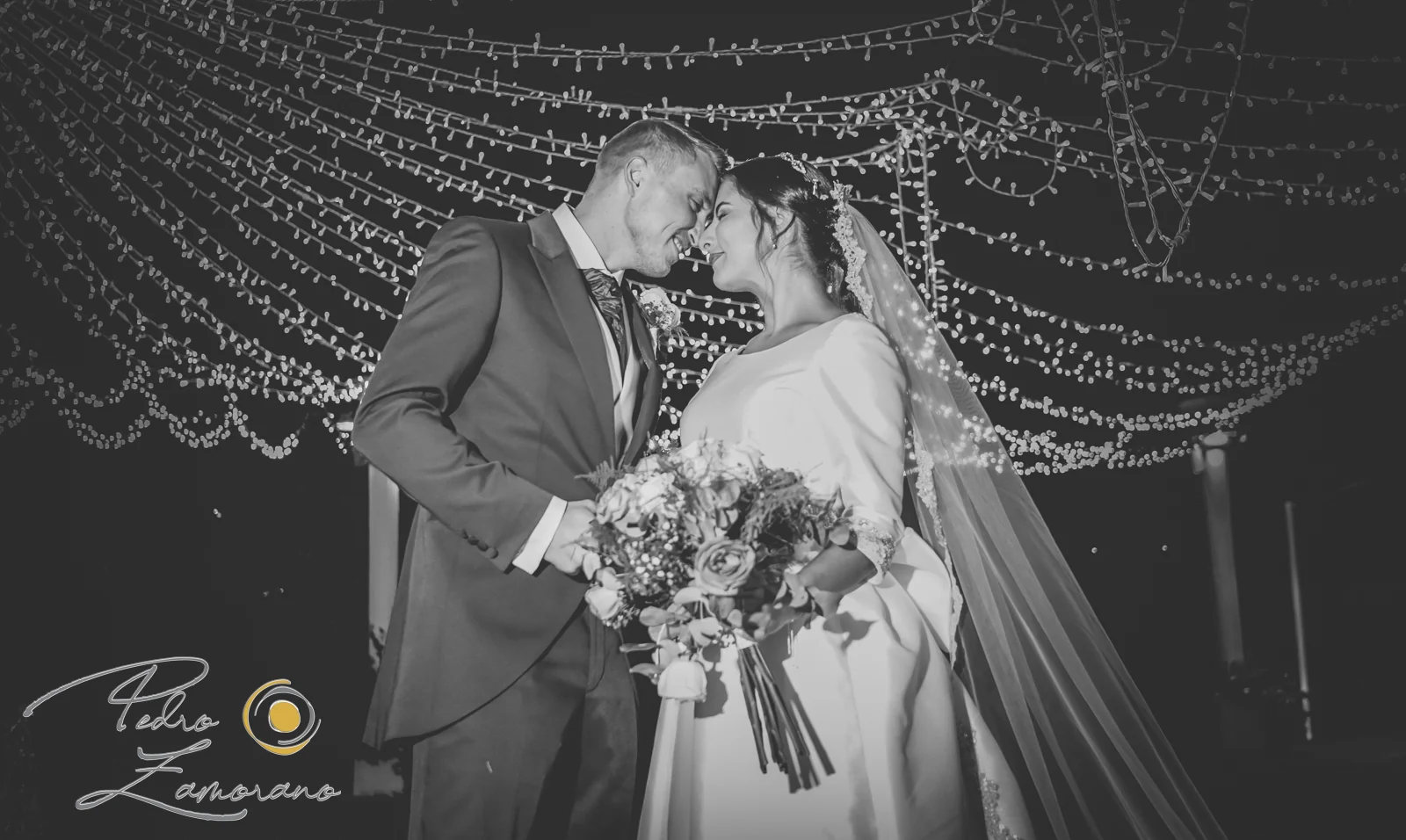 Novios de noche bajo guirnaldas en blanco y negro durante una boda en Mirador de Cuatro Vientos.